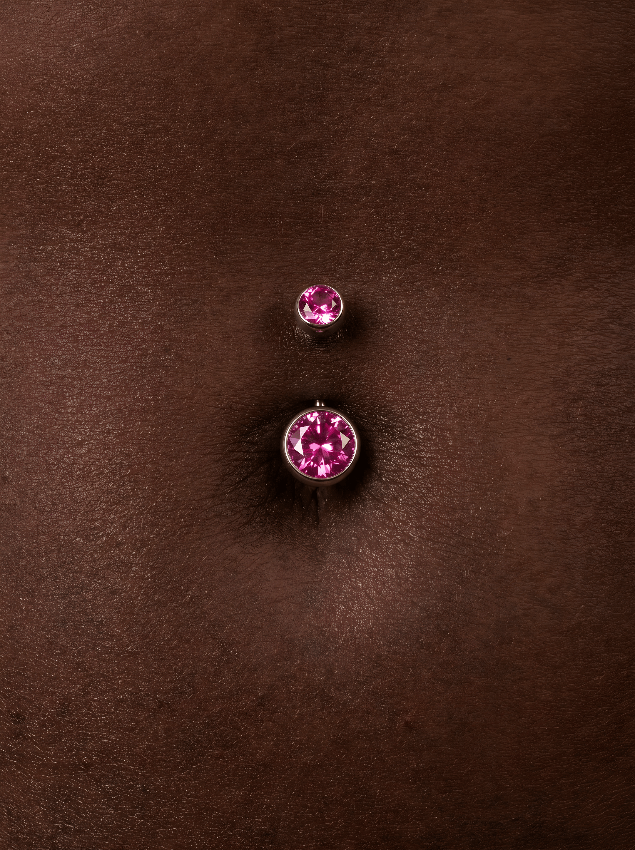 Primer plano de un ombligo adornado con el piercing para el ombligo «OMBLIGO CZ ROSA» de Titanio-Noble Art, con dos tachuelas de circonita cúbica rosa engastadas en plata chapada sobre una piel de color marrón oscuro.