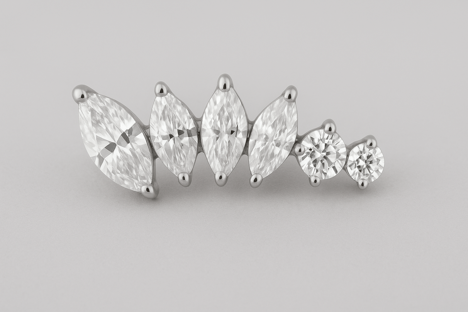 TOP ALICIA, de NOBLE ART BEAUTY SOCIEDAD LIMITADA, es un pendiente de diamantes con tres diamantes de talla marquesa y dos de talla redonda dispuestos en fila, engastados en plata u oro blanco, ideal para aportar elegancia tras la perforación, que se muestra sobre un fondo gris claro.