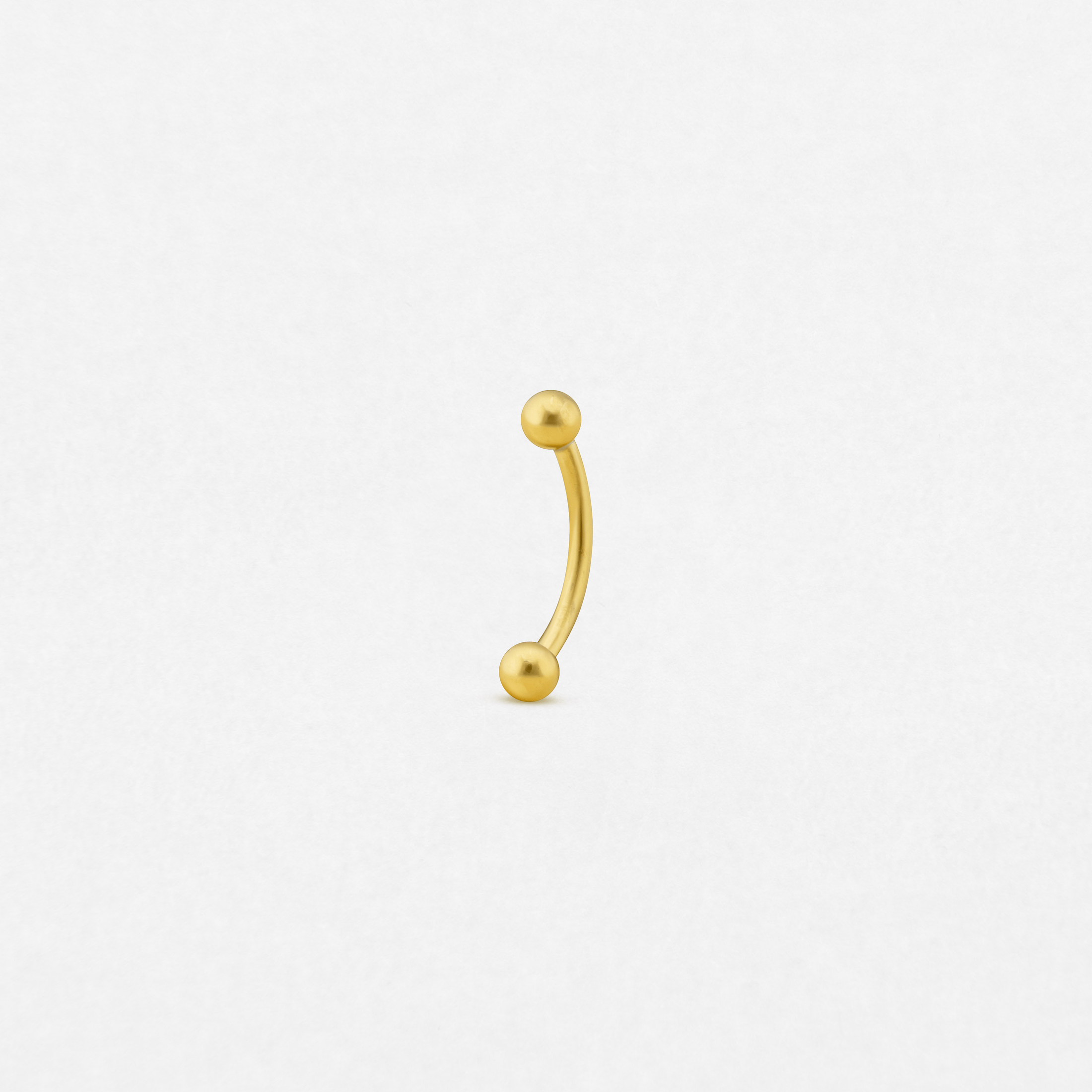 The «Banana» by NOBLE ART BEAUTY SOCIEDAD LIMITADA is a small gold curved barbell piercing with round ball ends, centered on a plain white background.