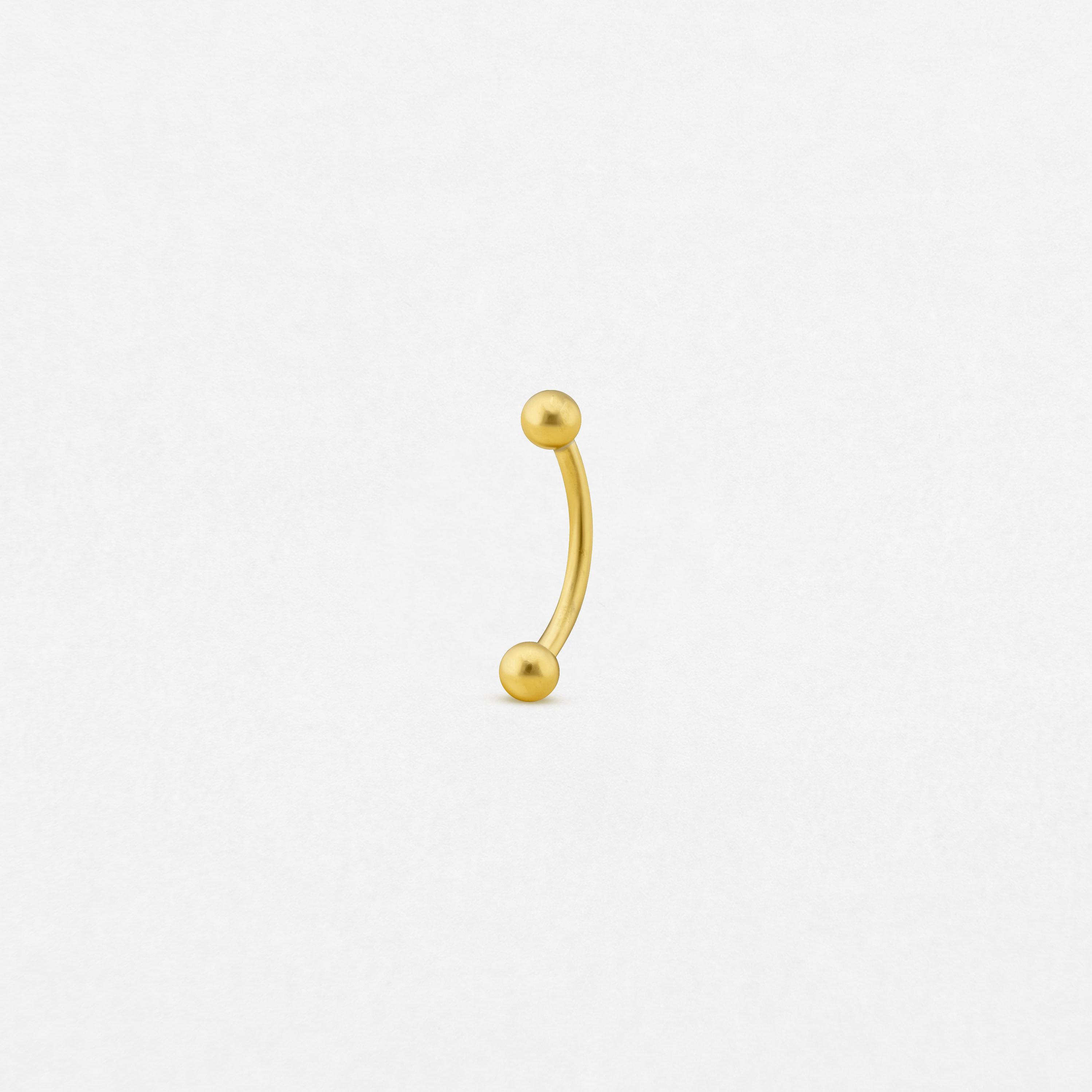 El «Banana» de NOBLE ART BEAUTY SOCIEDAD LIMITADA es un pequeño piercing tipo barra curvada de oro con extremos redondos en forma de bola, situado en el centro de un fondo blanco liso.