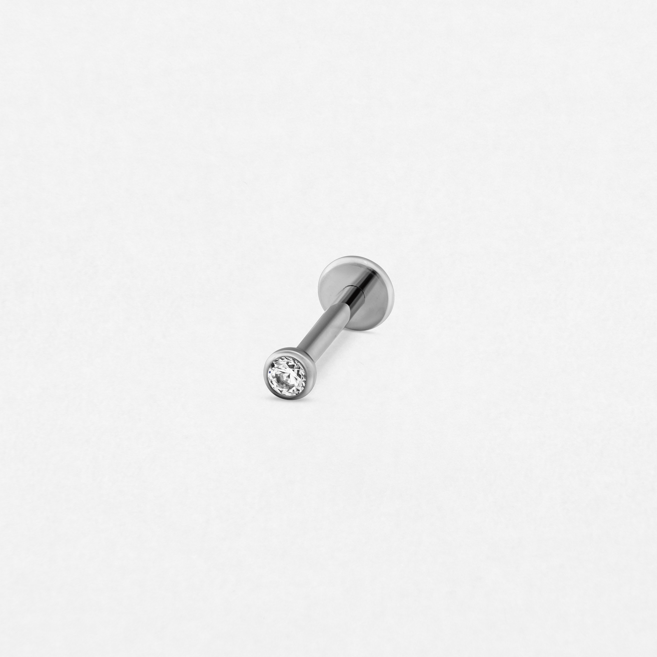 El pendiente tipo labret «CIRCONITA BLANCA» de Titanio-Noble Art cuenta con una gema redonda transparente y se muestra sobre un fondo blanco liso.