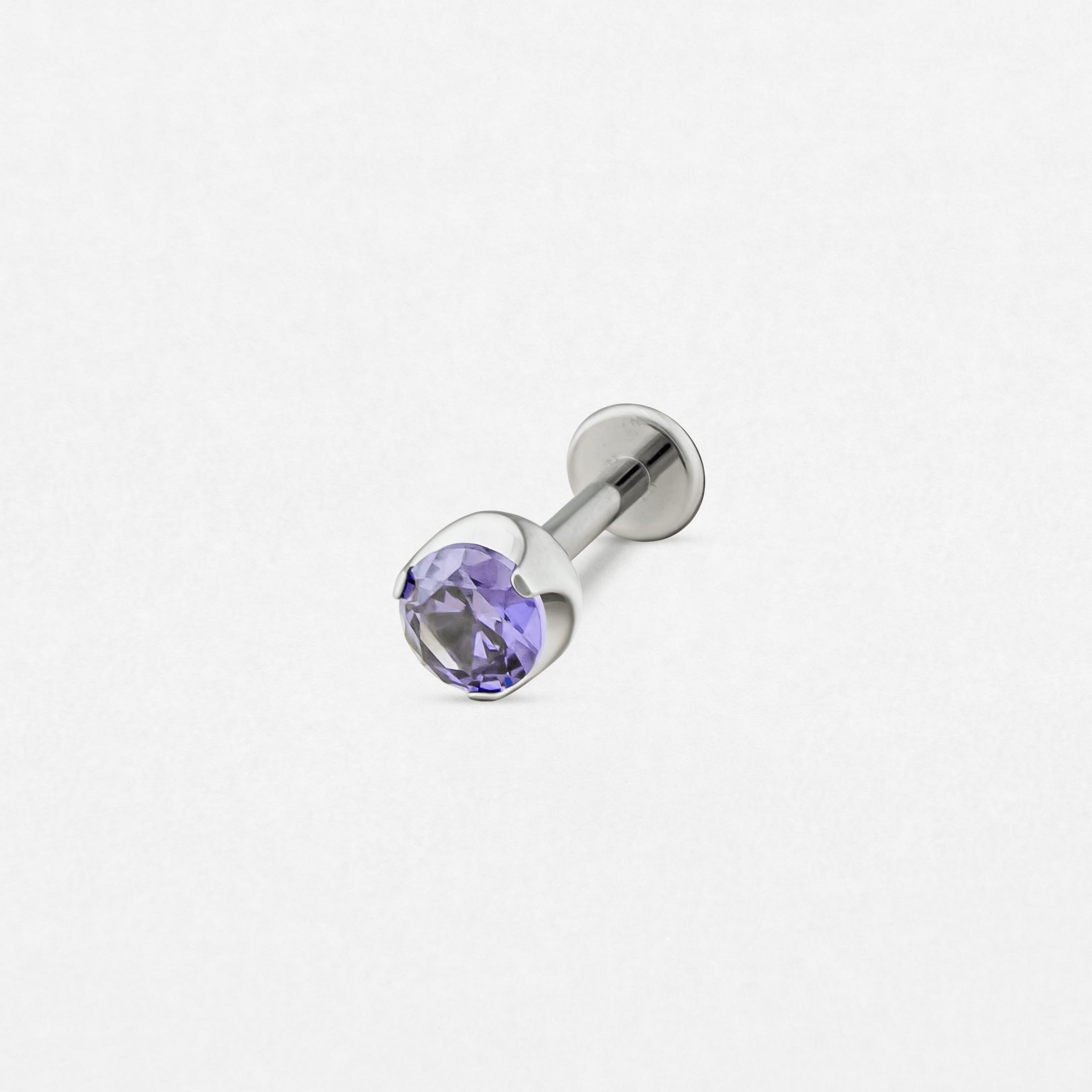 El «Circonita morada» de Titanio-Noble Art es un pendiente tipo labret de plata con una gema redonda y facetada de color morado claro engastada en garras, perfecto para tu colección de piercings y que se muestra sobre un fondo blanco.