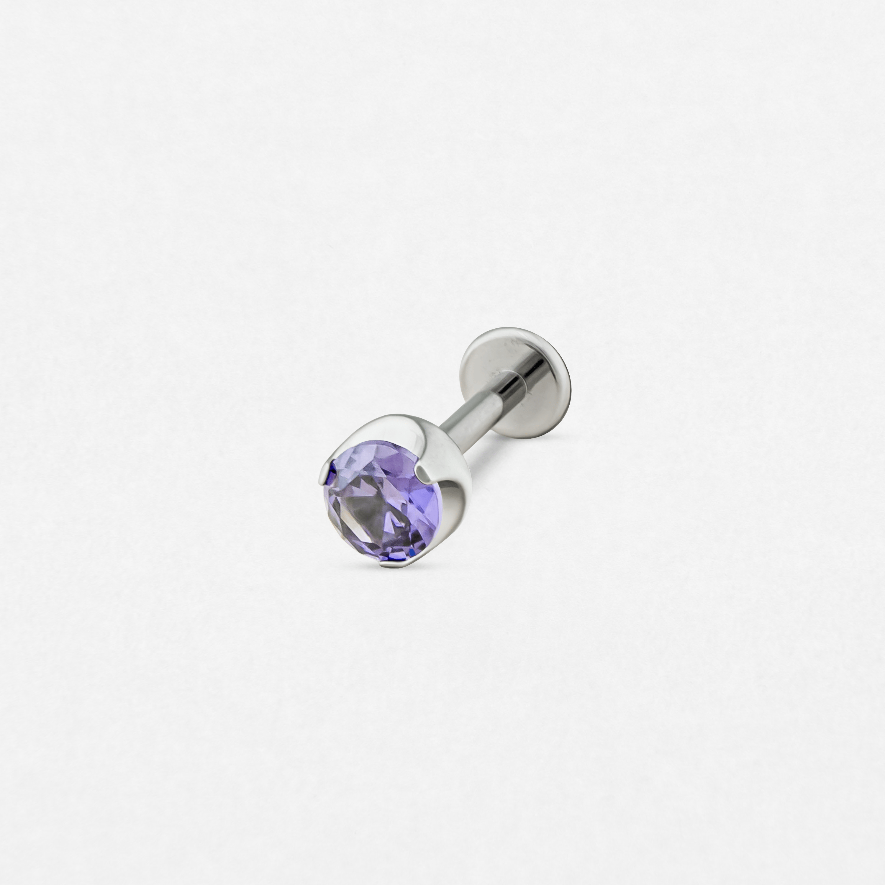 El «Circonita morada» de Titanio-Noble Art es un pendiente tipo labret de plata con una gema redonda y facetada de color morado claro engastada en garras, perfecto para tu colección de piercings y que se muestra sobre un fondo blanco.