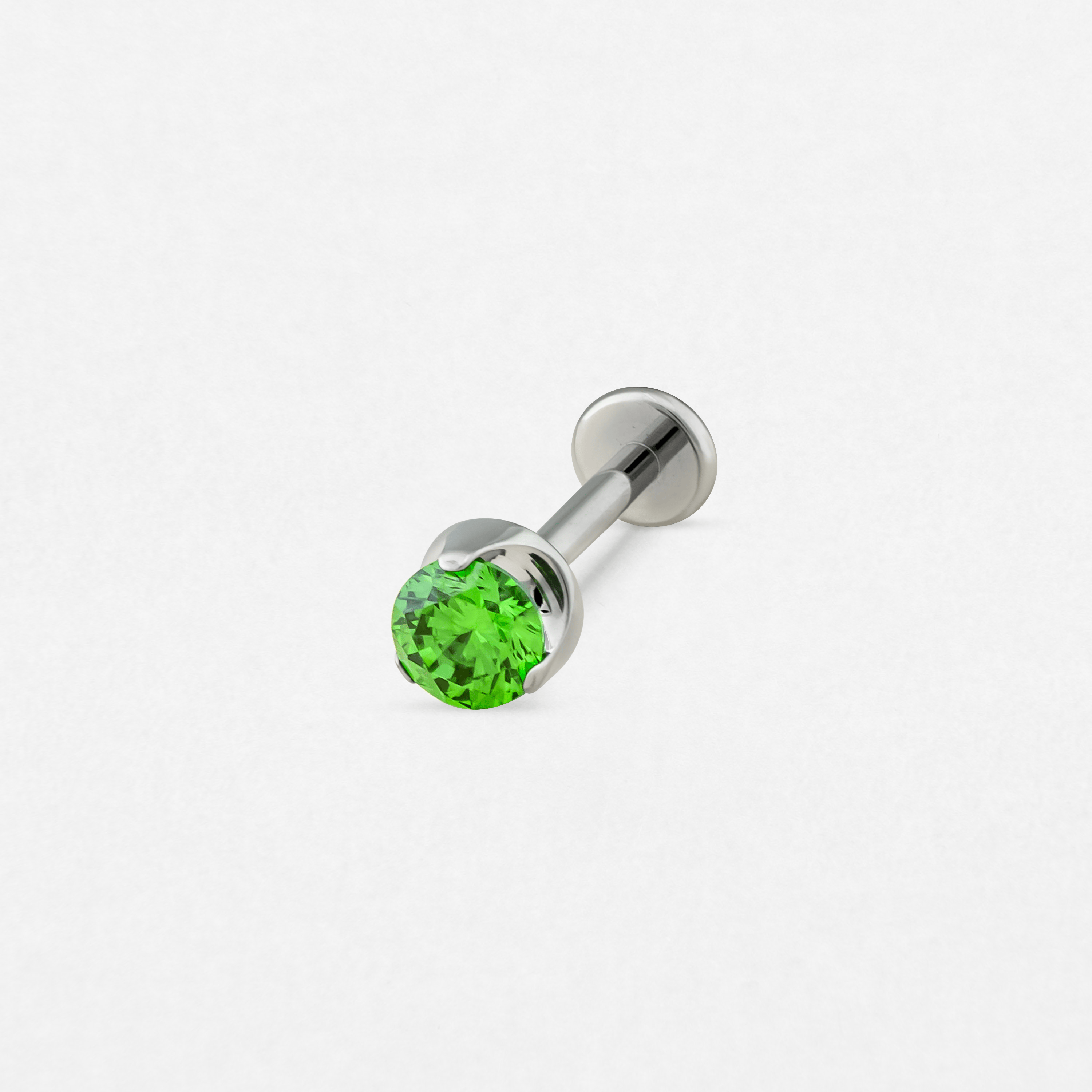 El «Circonita verde» de Titanio-Noble Art es un pendiente tipo labret de plata con una gema verde redonda y facetada en un extremo y un disco plano en el otro, que se muestra sobre un fondo blanco liso.