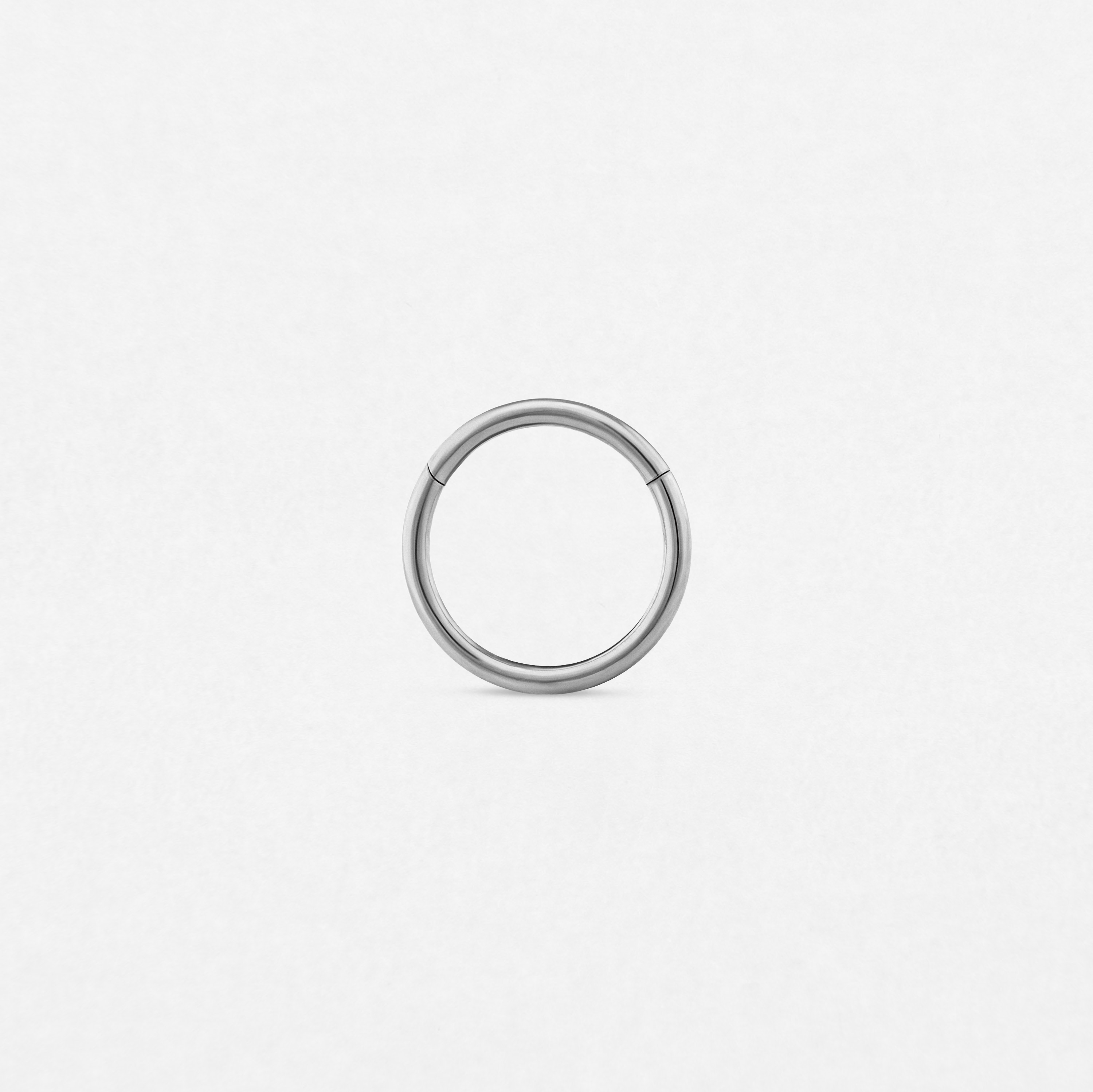 El Titanio- Noble Art Clicker es un sencillo aro metálico circular con un diseño sin costuras, perfecto para piercings, que se muestra sobre un fondo blanco liso.