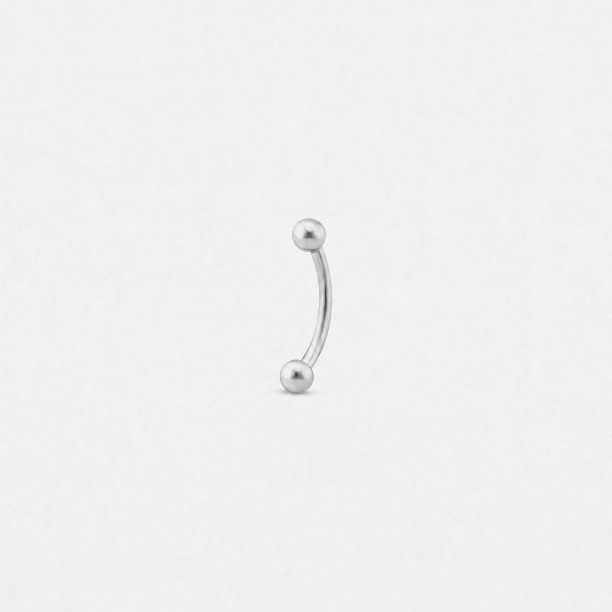 El modelo «The Banana» de NOBLE ART BEAUTY SOCIEDAD LIMITADA es una barra curva de plata con bolas metálicas en cada extremo, sobre un fondo blanco: ideal para lucir tu estilo Noble Art o para combinarla con un nuevo tatuaje.