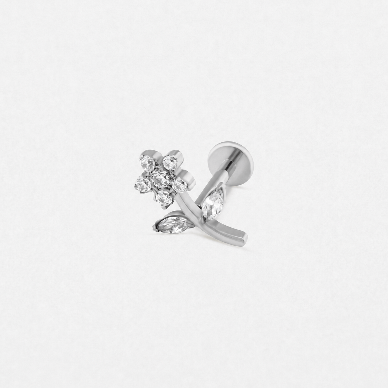 Los pendientes de botón de plata «Selena» de Titanio-Noble Art presentan un diseño floral con brillantes piedras preciosas transparentes en cada pétalo y hoja, lo que aporta elegancia a tu piercing. Se muestran sobre un fondo blanco liso.