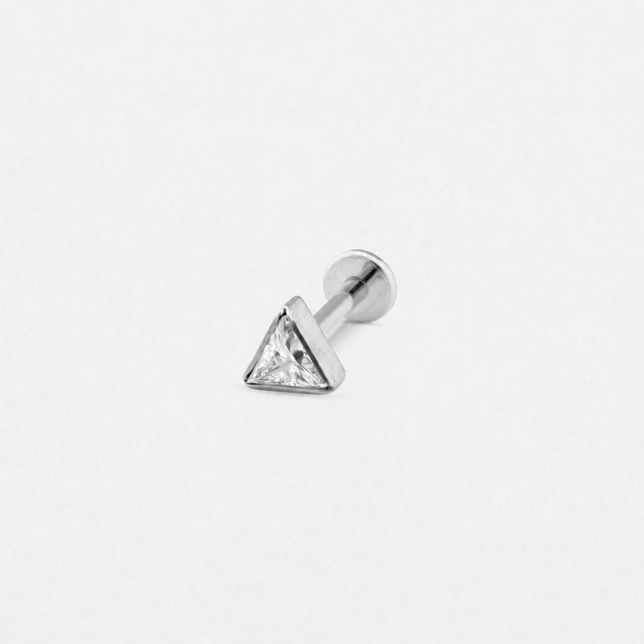 El pendiente «Titin» de Titanio-Noble Art es un pendiente de botón de plata con una piedra preciosa triangular transparente, que se muestra sobre un fondo blanco liso.