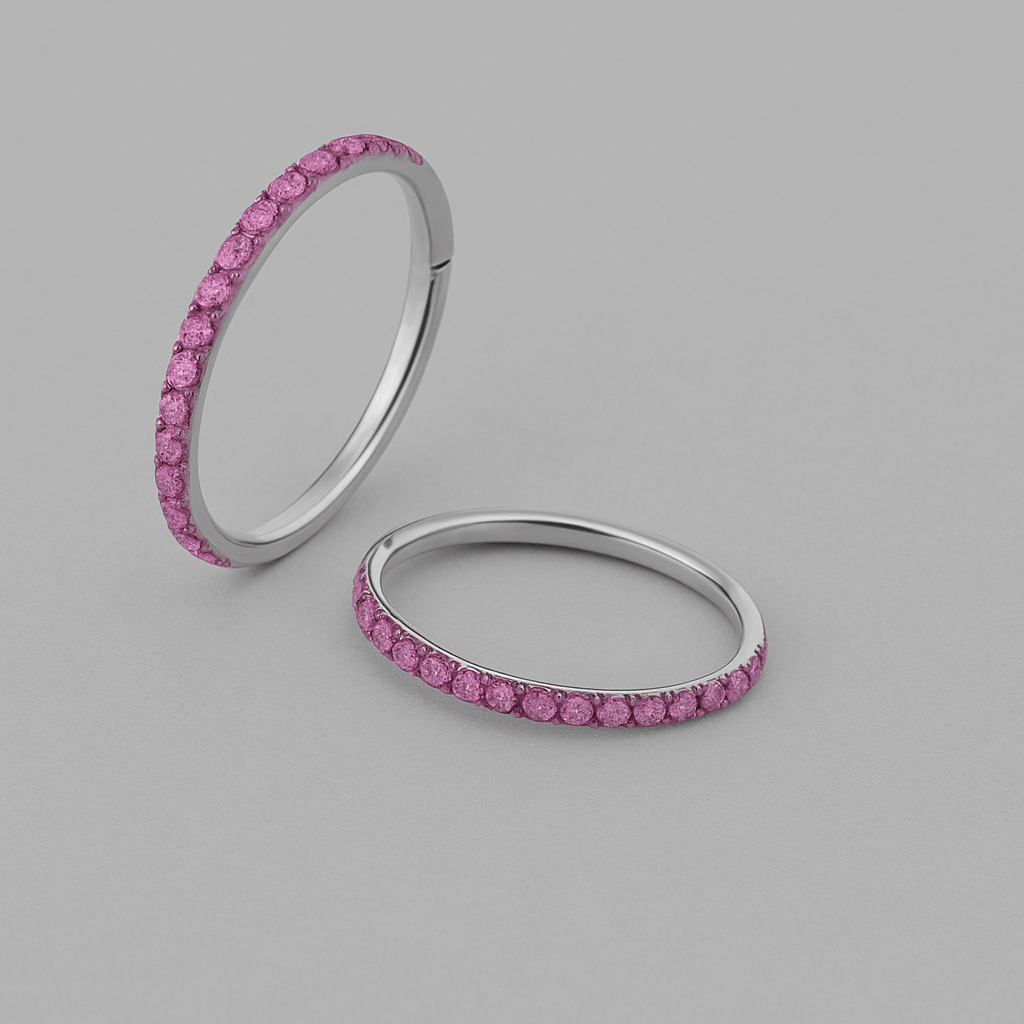 Se muestran dos anillos EMILY PINK plateados y finos de NOBLE ART BEAUTY SOCIEDAD LIMITADA, cada uno con una banda continua de piedras preciosas de color rosa; uno en posición horizontal y otro en posición vertical, sobre un fondo gris claro.