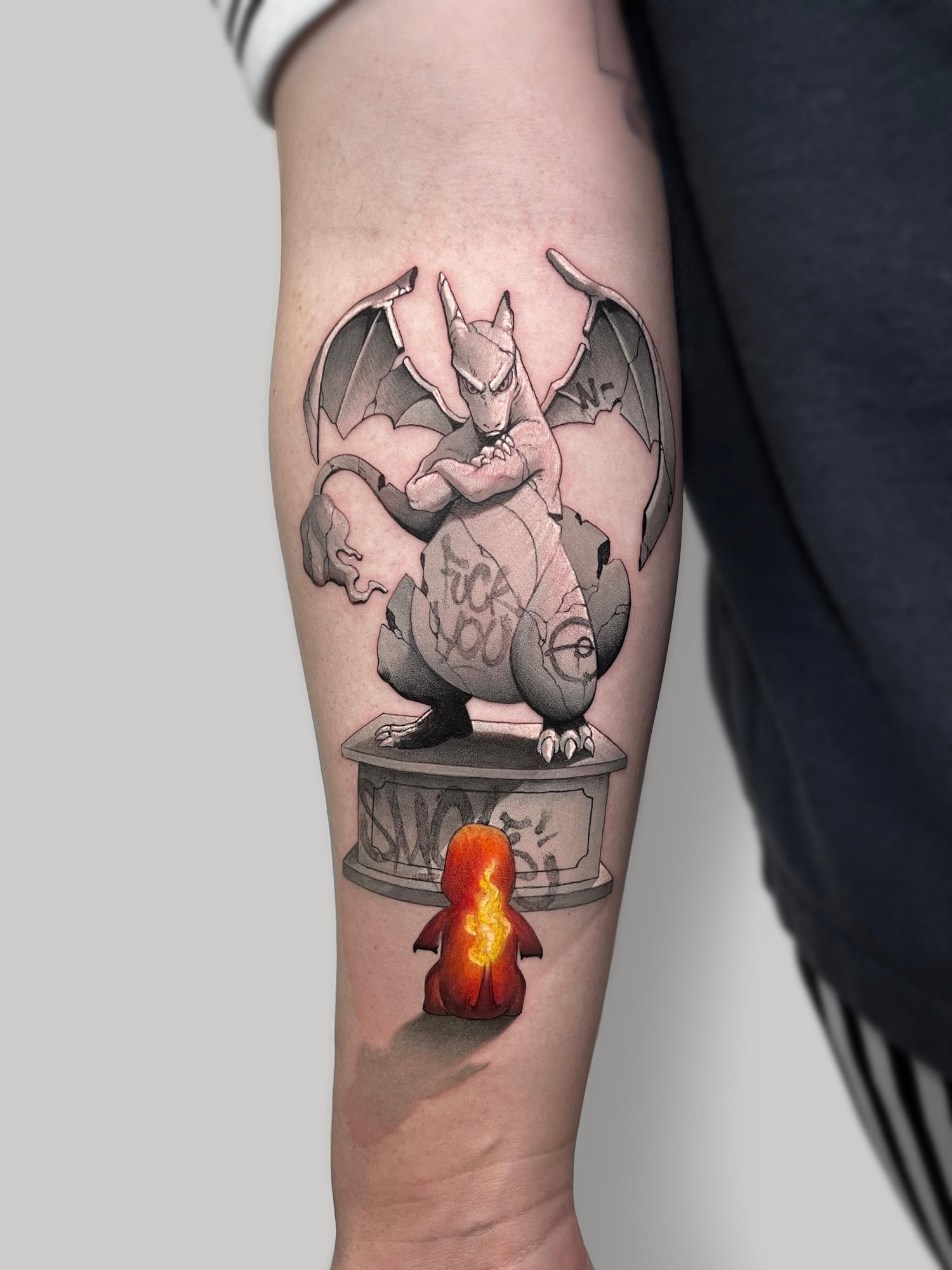 Un pequeño tatuaje de Charmander frente a una estatua de Charizard, sombreado en negro y gris con texto de grafiti, en el antebrazo: una auténtica obra de Noble Art. Para futuros cambios, ten en cuenta la opción de Matias Noble, de NOBLE ART OFFICIAL COORP: eliminación con láser en 1 año.