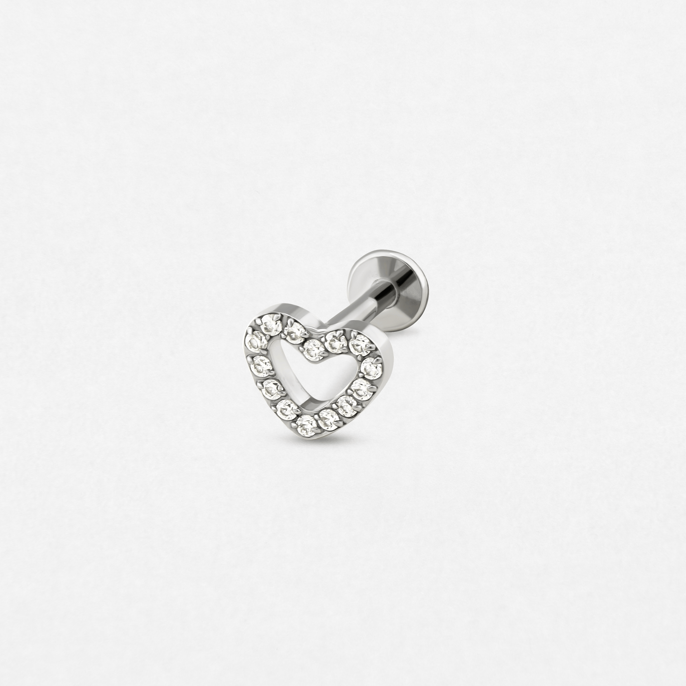 El «Love liso» de Titanio-Noble Art es un pendiente de labret de plata con un diseño en forma de corazón adornado con pedrería transparente, ideal para tu próximo piercing, que se muestra sobre un fondo blanco liso.