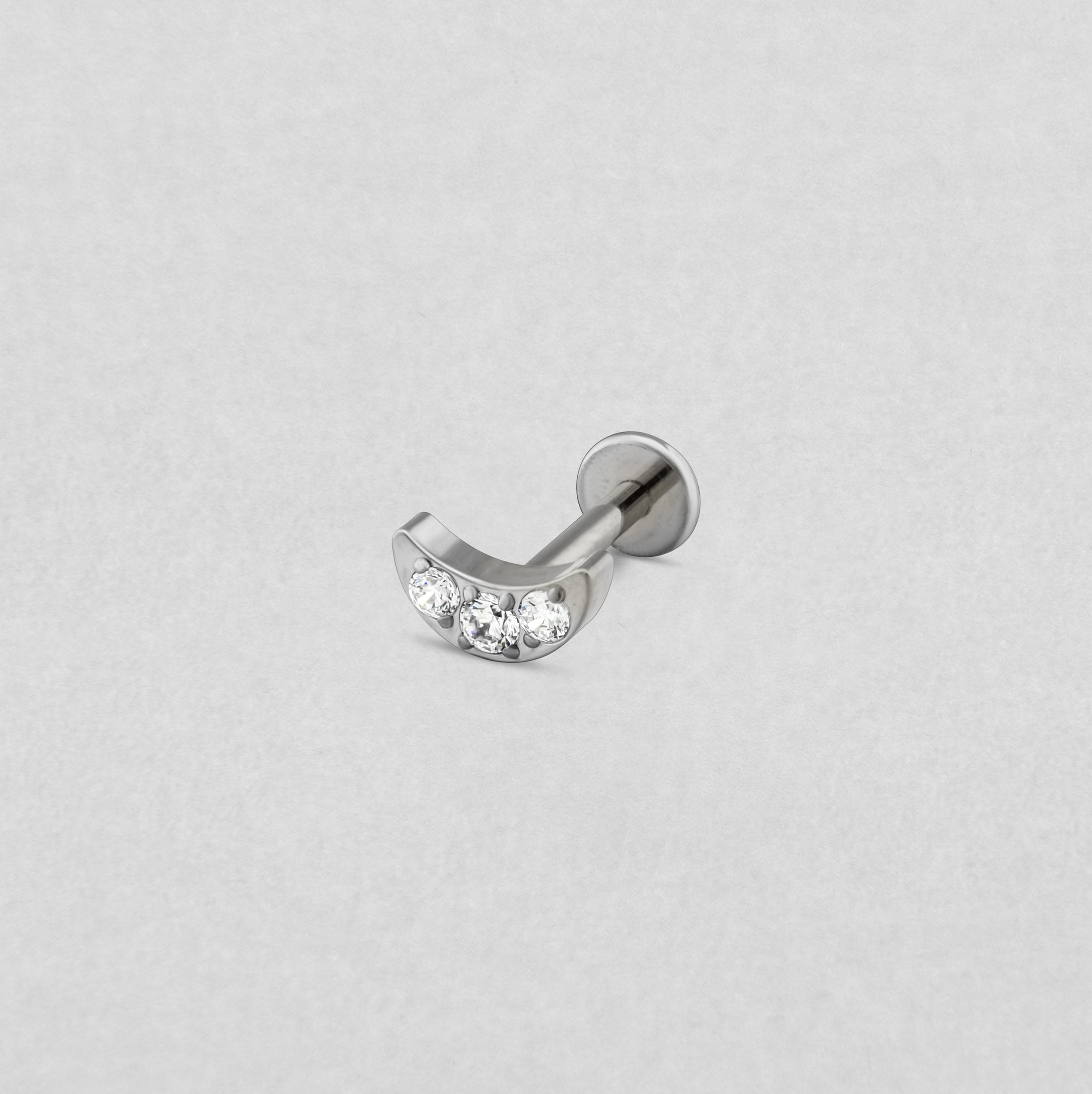 El «Titanio- Noble Art Moon cz» es una barra curva de plata con tres piedras preciosas transparentes engastadas en la curva, que se muestra sobre un fondo gris claro.