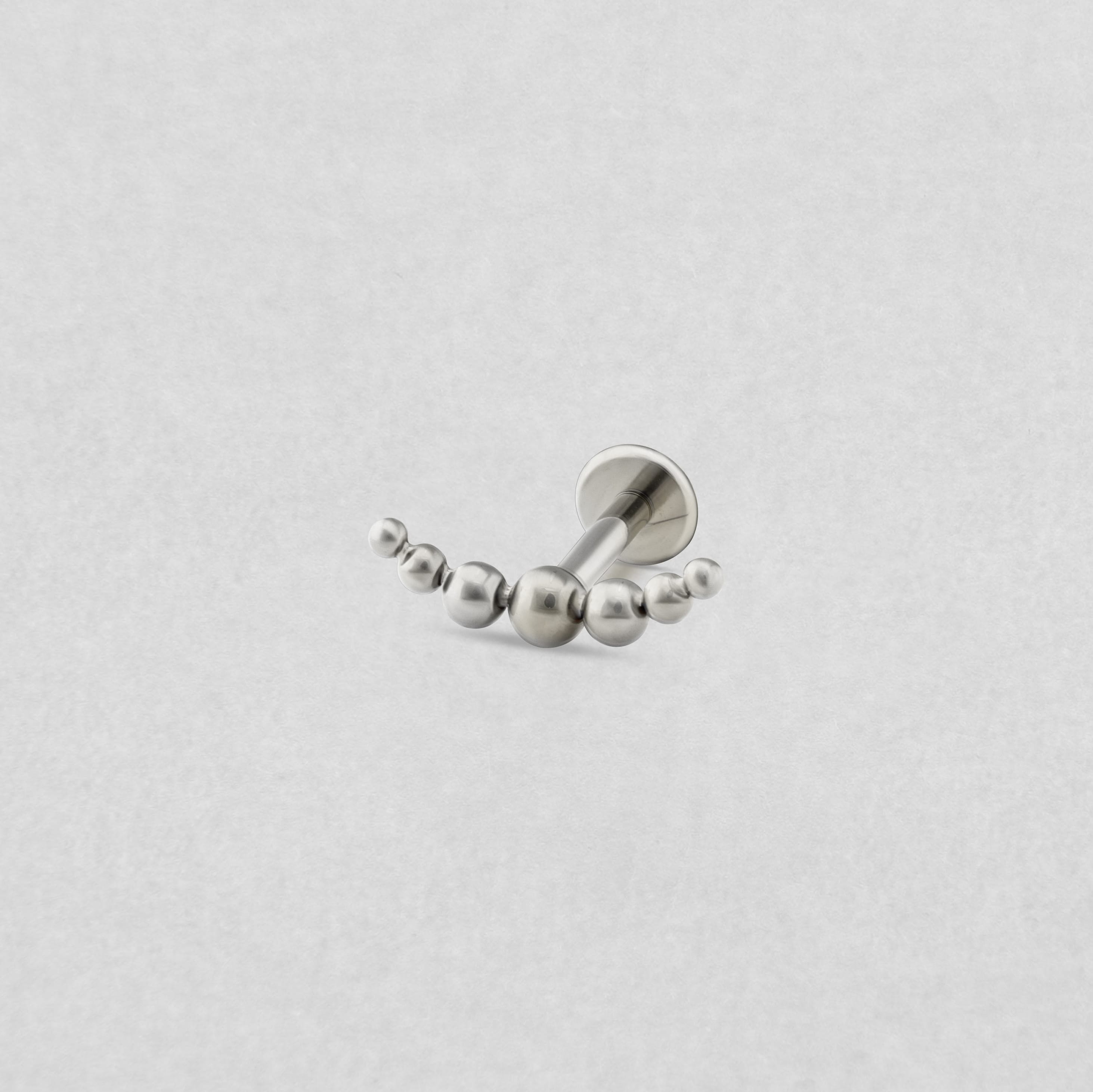 El modelo «Moon Cluster» de Titanio-Noble Art es un pendiente curvo de plata con un pendiente central y cuentas redondas de distintos tamaños, que se lucen con elegancia sobre un fondo blanco liso.