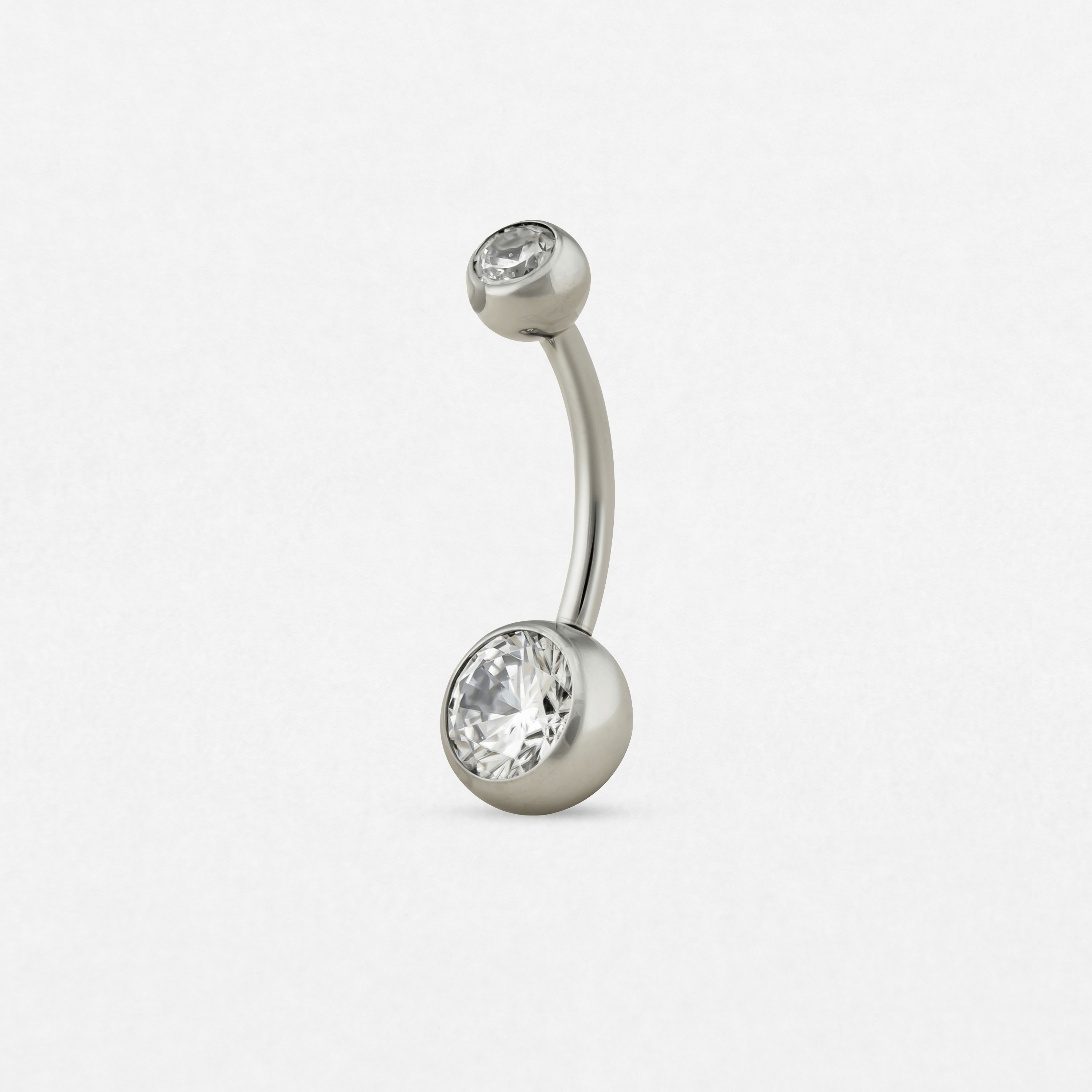 El «Ombligo cz silver» de Titanio-Noble Art es un piercing de plata curvado para el ombligo que cuenta con dos piedras preciosas redondas transparentes en cada extremo, sobre un fondo blanco: una opción elegante como nueva joya o antes de la eliminación con láser de un tatuaje antiguo.