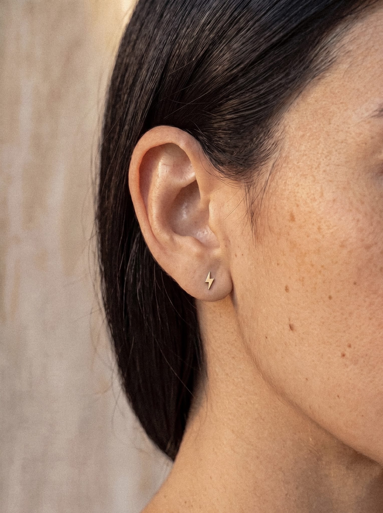 Primer plano de la oreja de una persona que lleva el pendiente de botón «Star liso» de Titanio-Noble Art, lo que pone de relieve su pasión por la joyería. La persona tiene la piel suave y bronceada y el pelo castaño oscuro recogido detrás de la oreja, lo que realza con elegancia este refinado piercing.