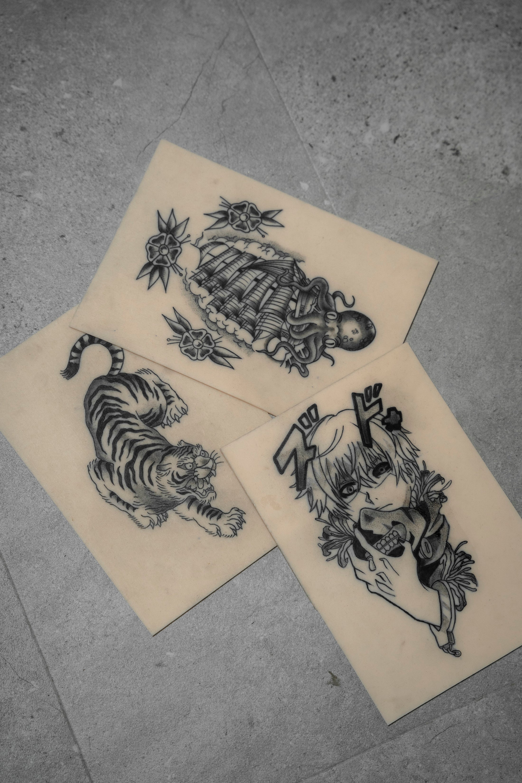 Tres hojas de diseños de tatuajes de Matias Noble, de NOBLE ART OFFICIAL COORP, en fondo gris, con una chica con flores, un tigre y un personaje de anime con una máscara de zorro y texto en japonés. Ideales para los fans de la colección «Noble Art - 1 semana».