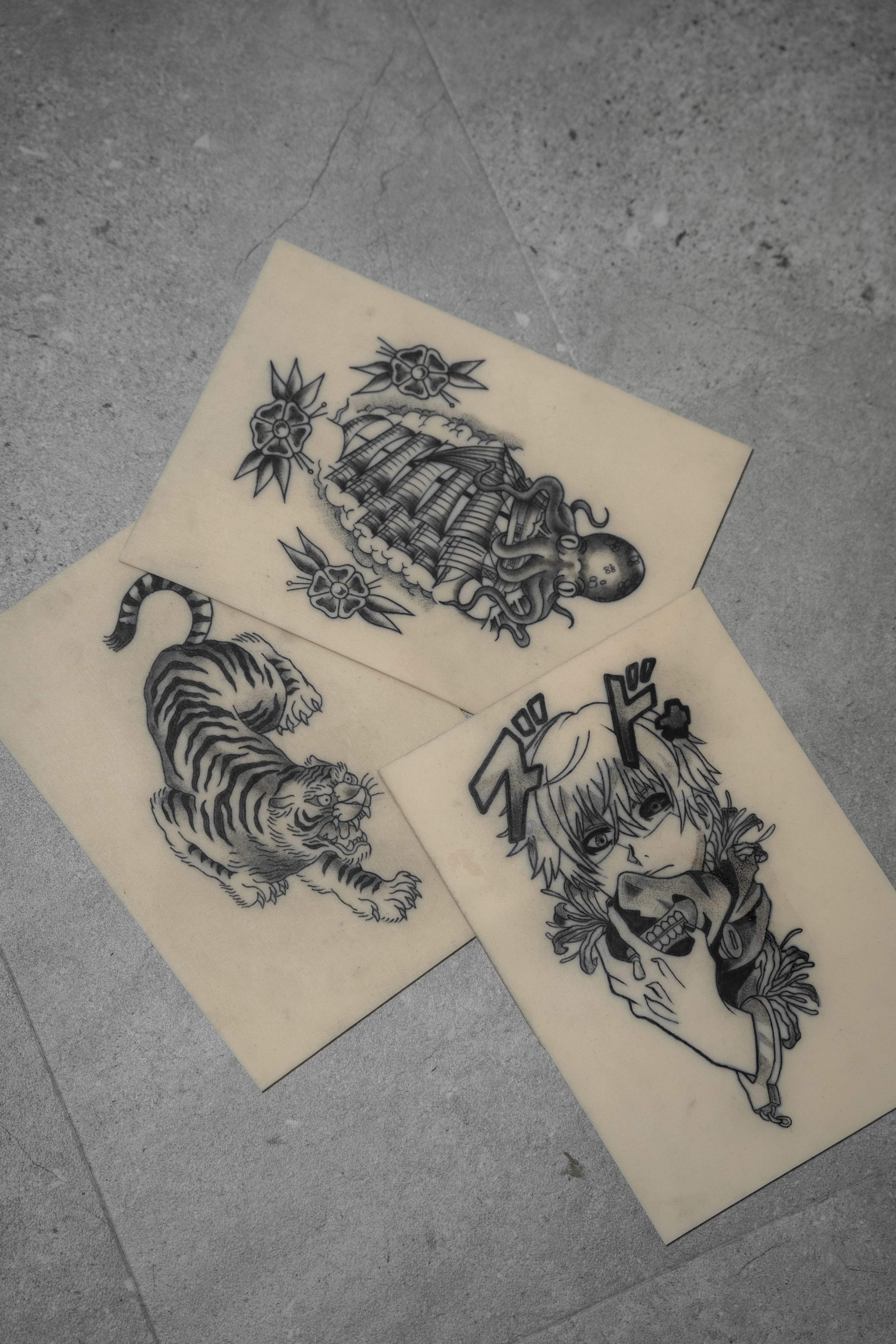 Tres hojas de diseños de tatuajes de Matias Noble, de NOBLE ART OFFICIAL COORP, en fondo gris, con una chica con flores, un tigre y un personaje de anime con una máscara de zorro y texto en japonés. Ideales para los fans de la colección «Noble Art - 1 semana».