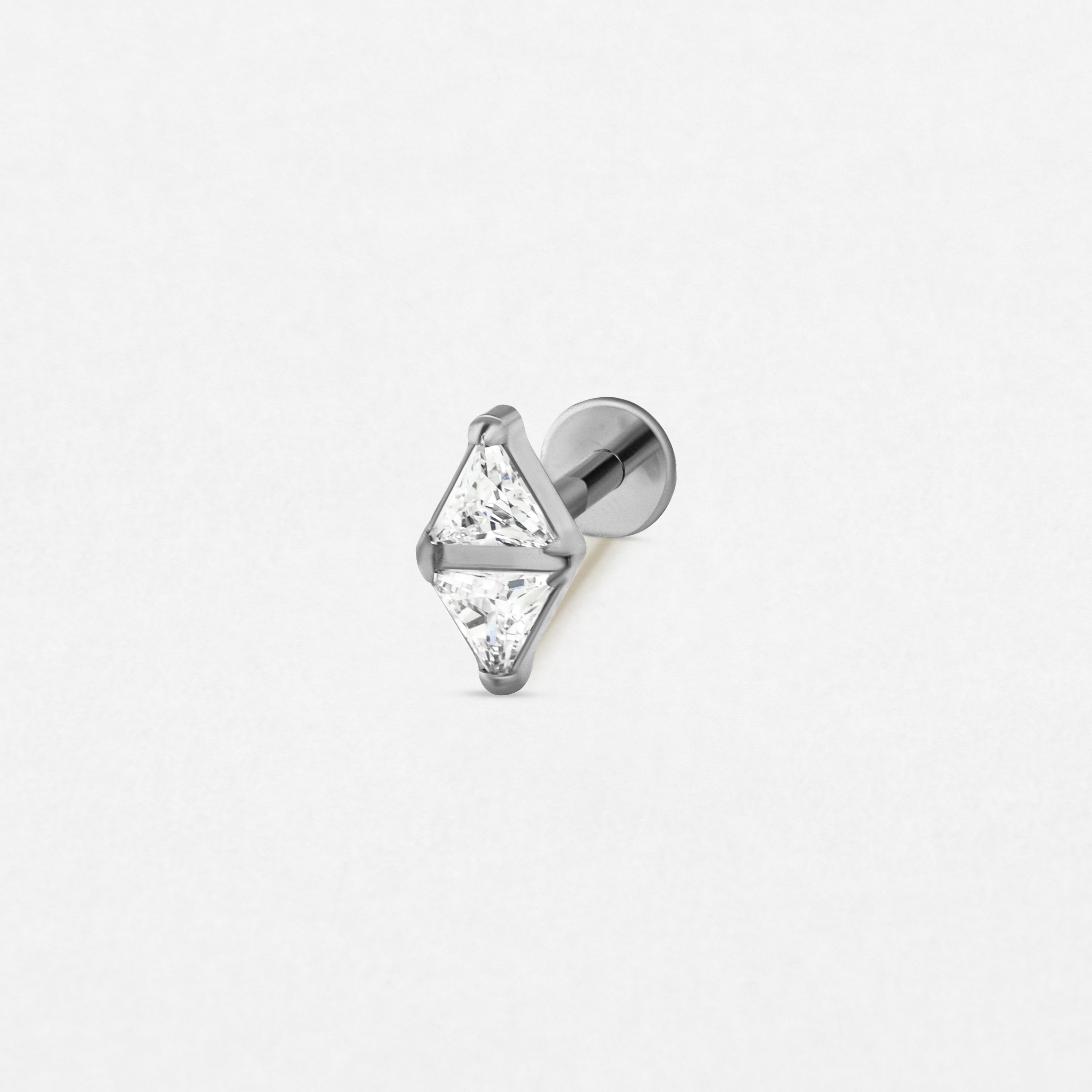 El pendiente «Anastasia» de Titanio-Noble Art cuenta con dos cristales transparentes triangulares engastados en forma de rombo sobre un pendiente de botón de plata con la parte trasera plana, ideal para perforaciones elegantes. Se muestra sobre un fondo blanco liso.