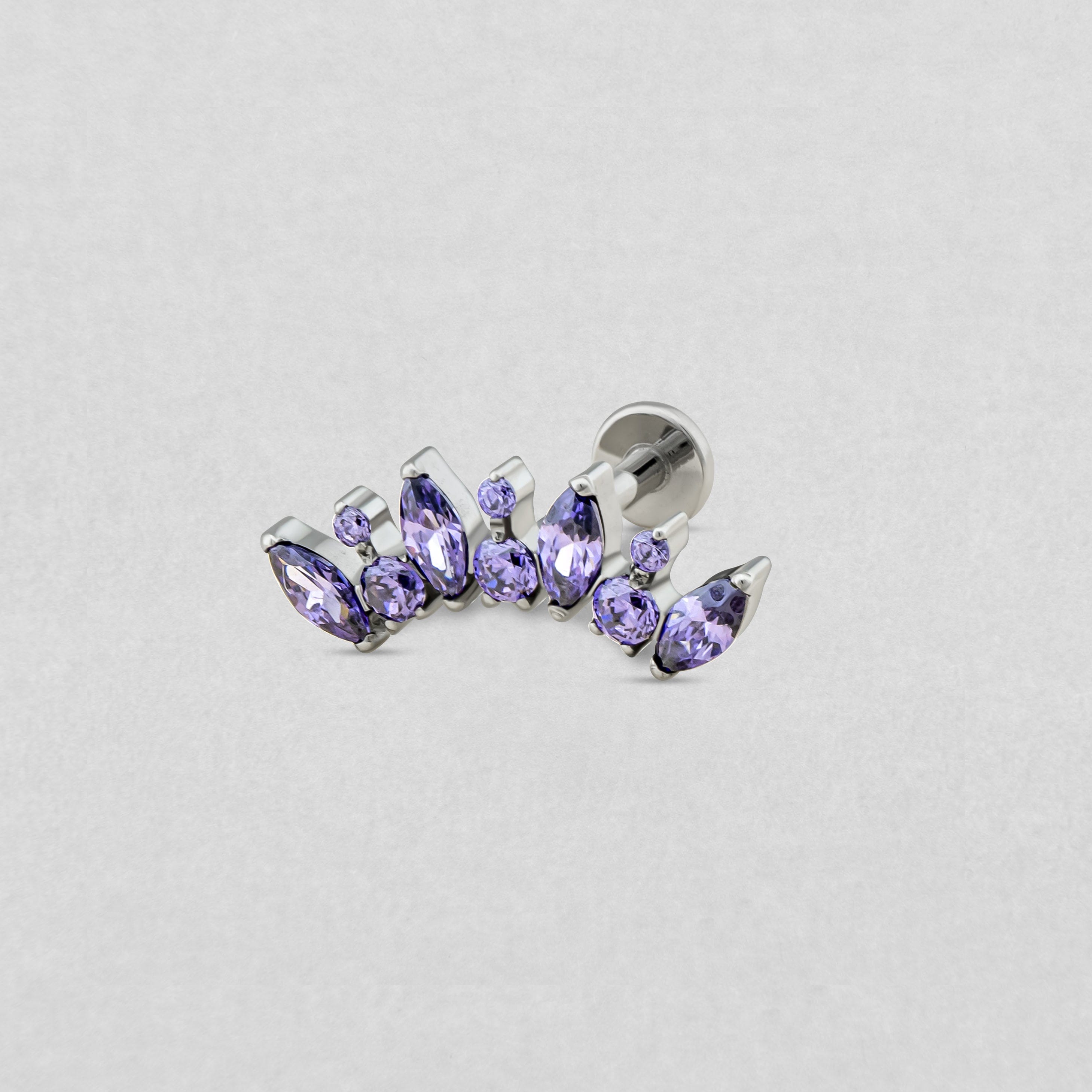 The Titanio–Noble Art "Apolo amatista" model is a silver earring with lavender-colored pear and round stones arranged in a gentle curve, presented against a light gray background: a true tribute to modern jewelry design.