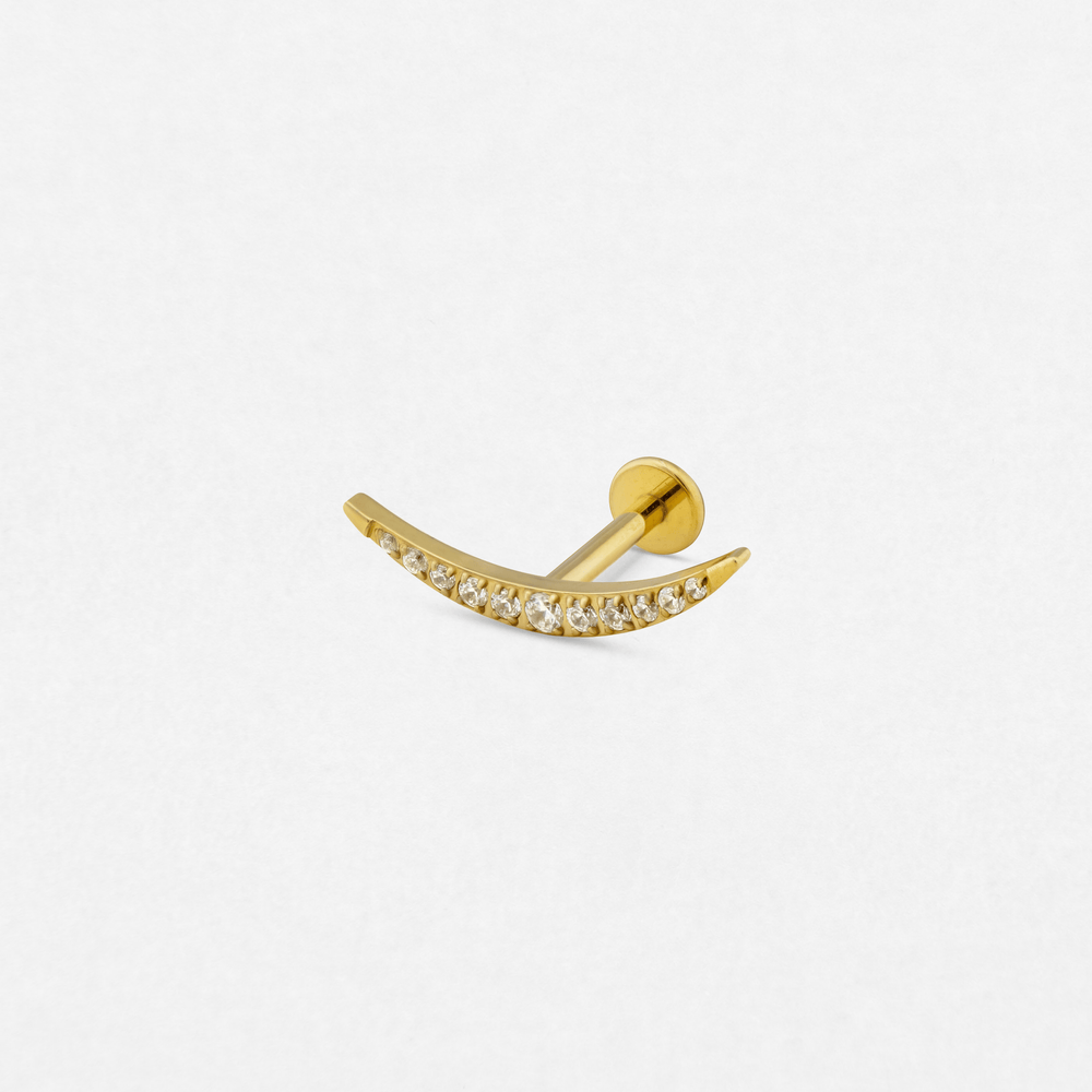 The «Atenea» model by Titanio-Noble Art is a curved gold stud earring with small transparent precious stones, ideal for fresh piercings, shown on a plain white background.