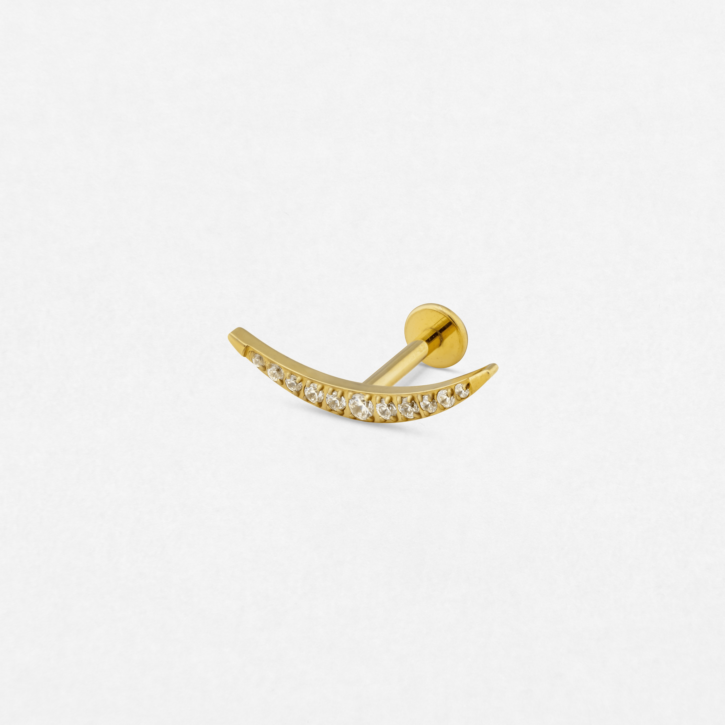 El modelo «Atenea» de Titanio-Noble Art es un pendiente de botón curvo de oro con pequeñas piedras preciosas transparentes, ideal para perforaciones recientes, que se muestra sobre un fondo blanco liso.