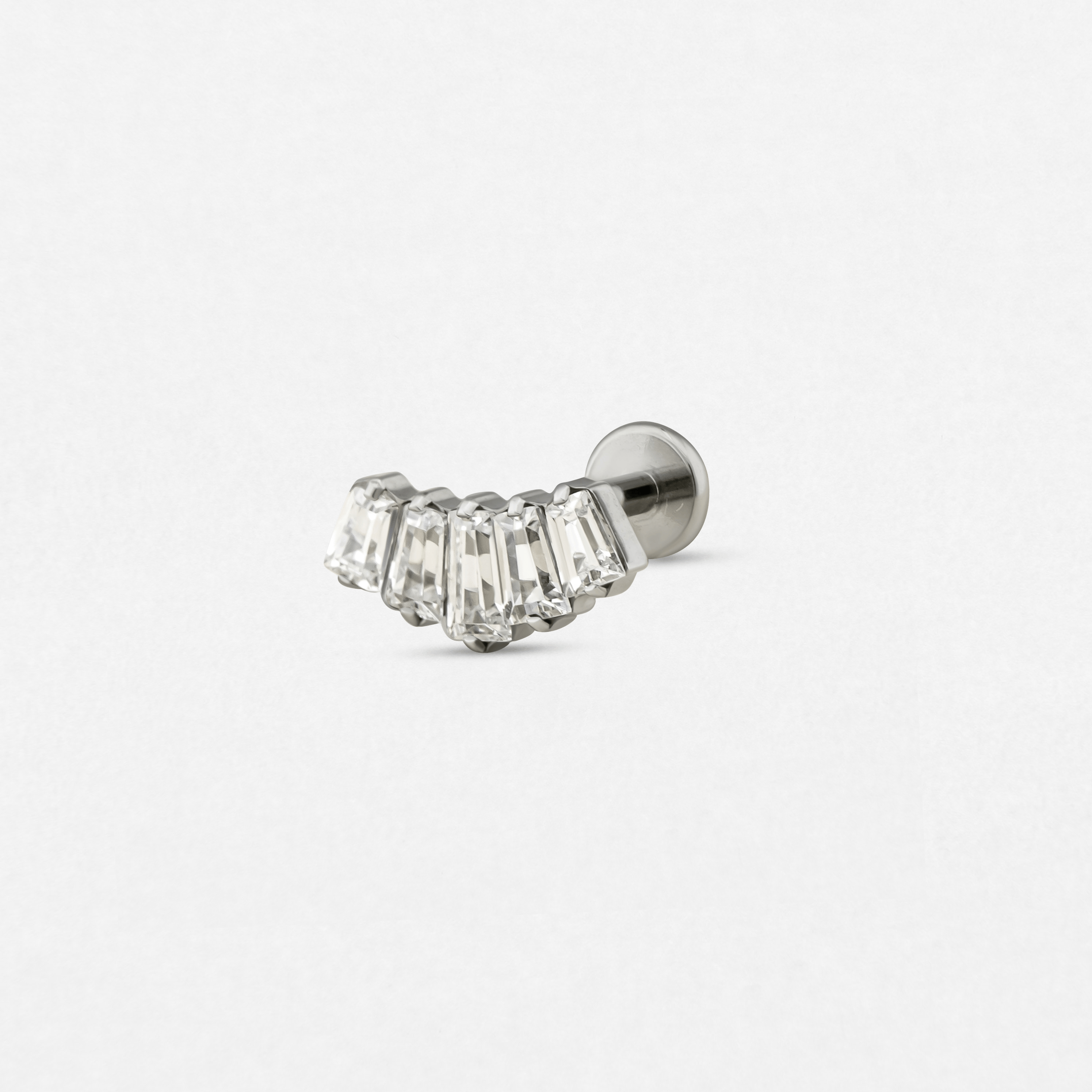 El pendiente «Baguette» de Titanio-Noble Art es un pendiente de plata de un solo pendiente que presenta una fila curvada de cinco piedras preciosas rectangulares transparentes engastadas una al lado de la otra, lo que aporta un elegante brillo a tu piercing. Se muestra sobre un fondo blanco liso.