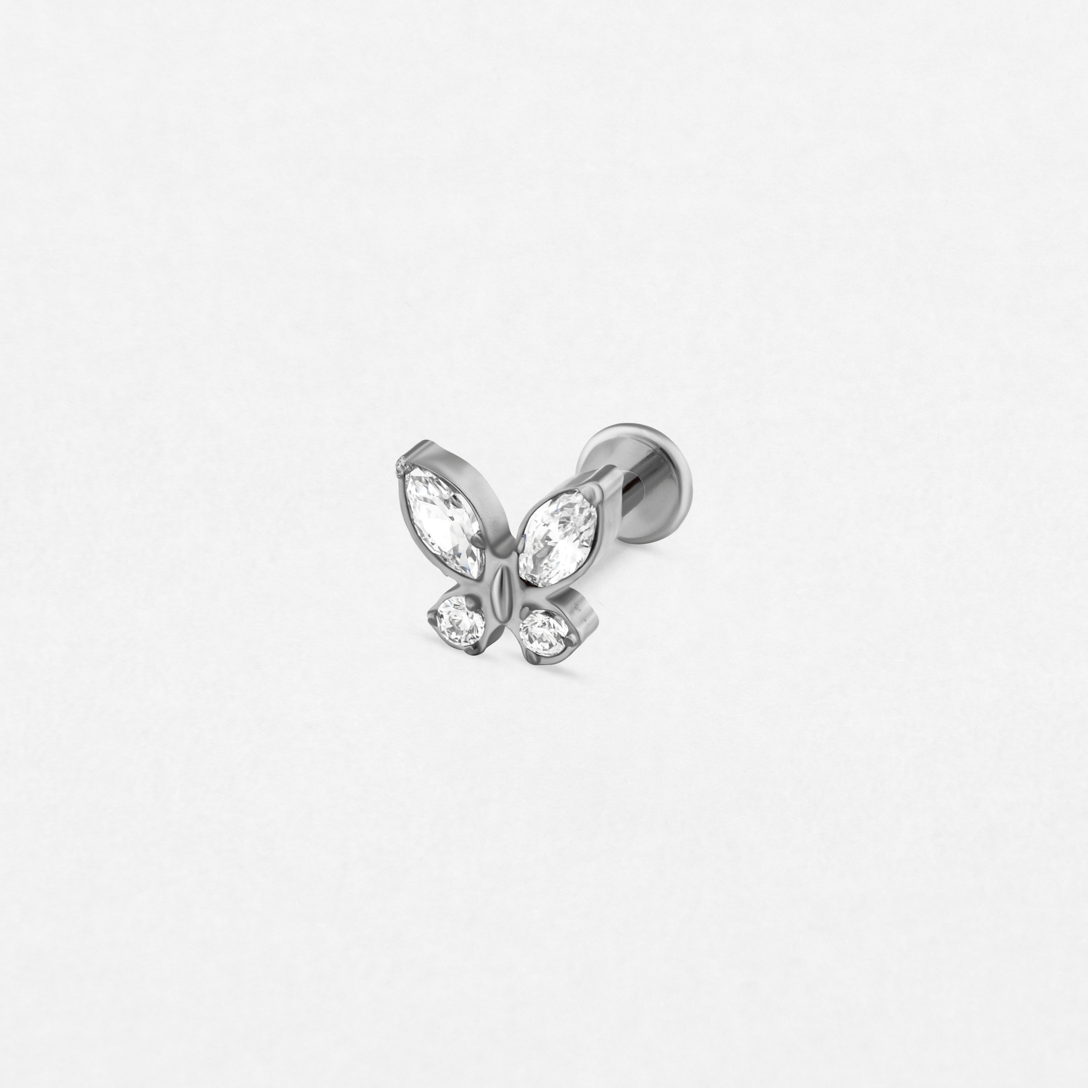 El modelo «Butterfly Silver» de Titanio-Noble Art es un pequeño pendiente de botón de plata con cuatro alas de piedras preciosas transparentes en forma de mariposa, ideal para cualquier tipo de piercing, que se muestra sobre un fondo blanco liso.