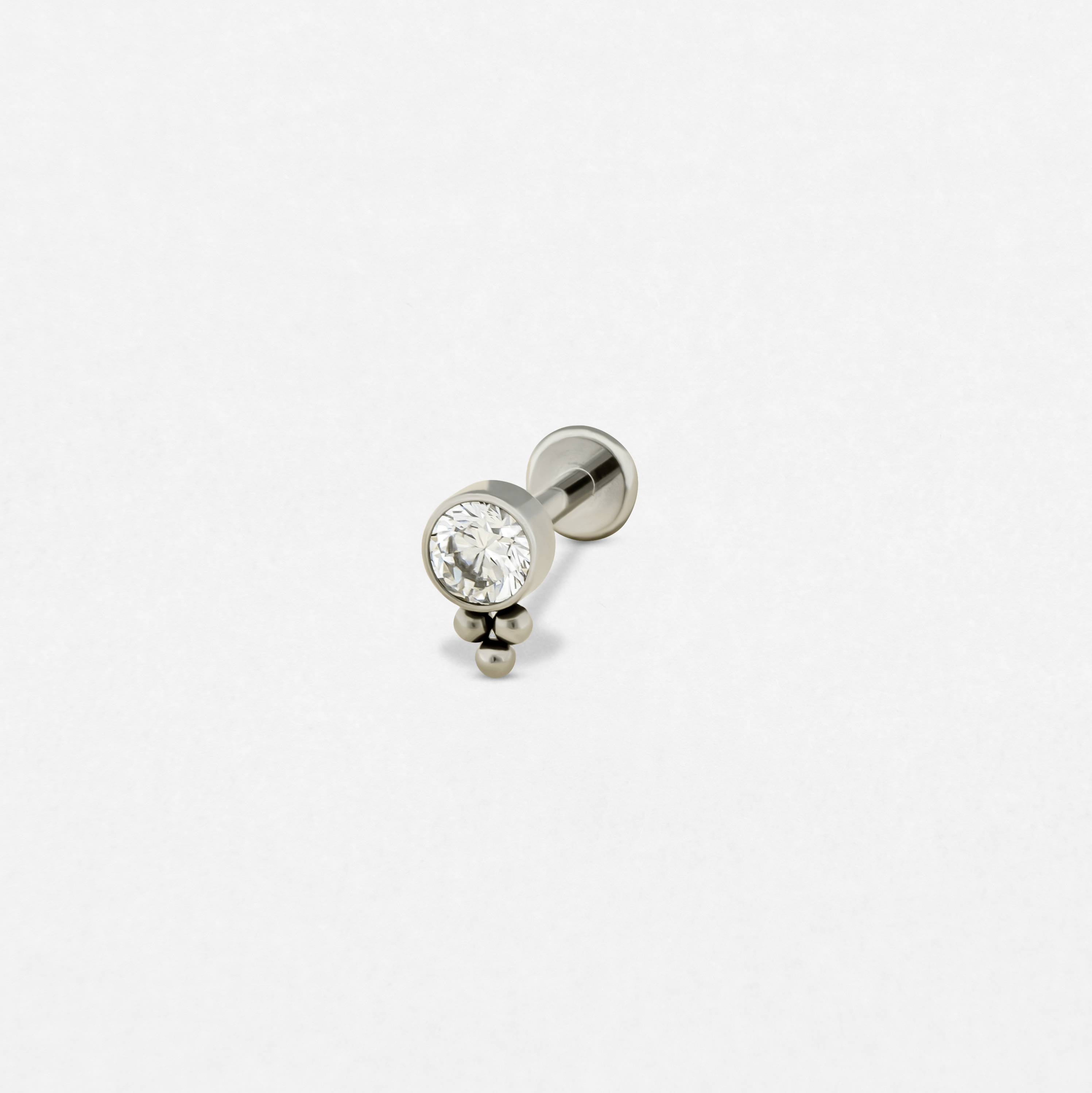 The «Destello simple» model by Titanio-Noble Art is a silver stud earring with a large round transparent precious stone and two small silver beads below, ideal for any type of piercing, shown on a plain white background.
