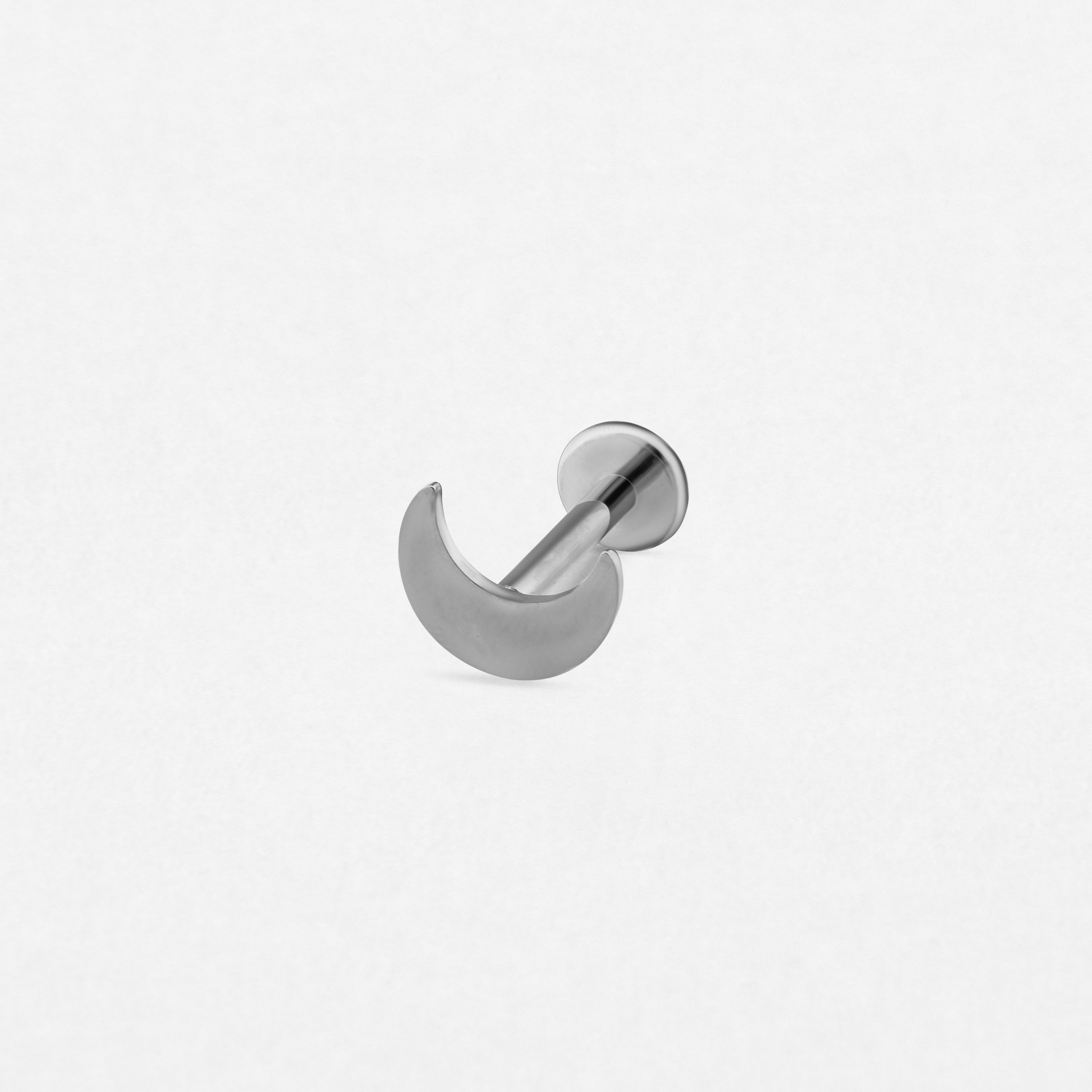 The «Eclipse» stud earring by NOBLE ART BEAUTY SOCIEDAD LIMITADA features a silver crescent moon design and a flat circular back, ideal for fresh piercings. Shown on a plain white background.