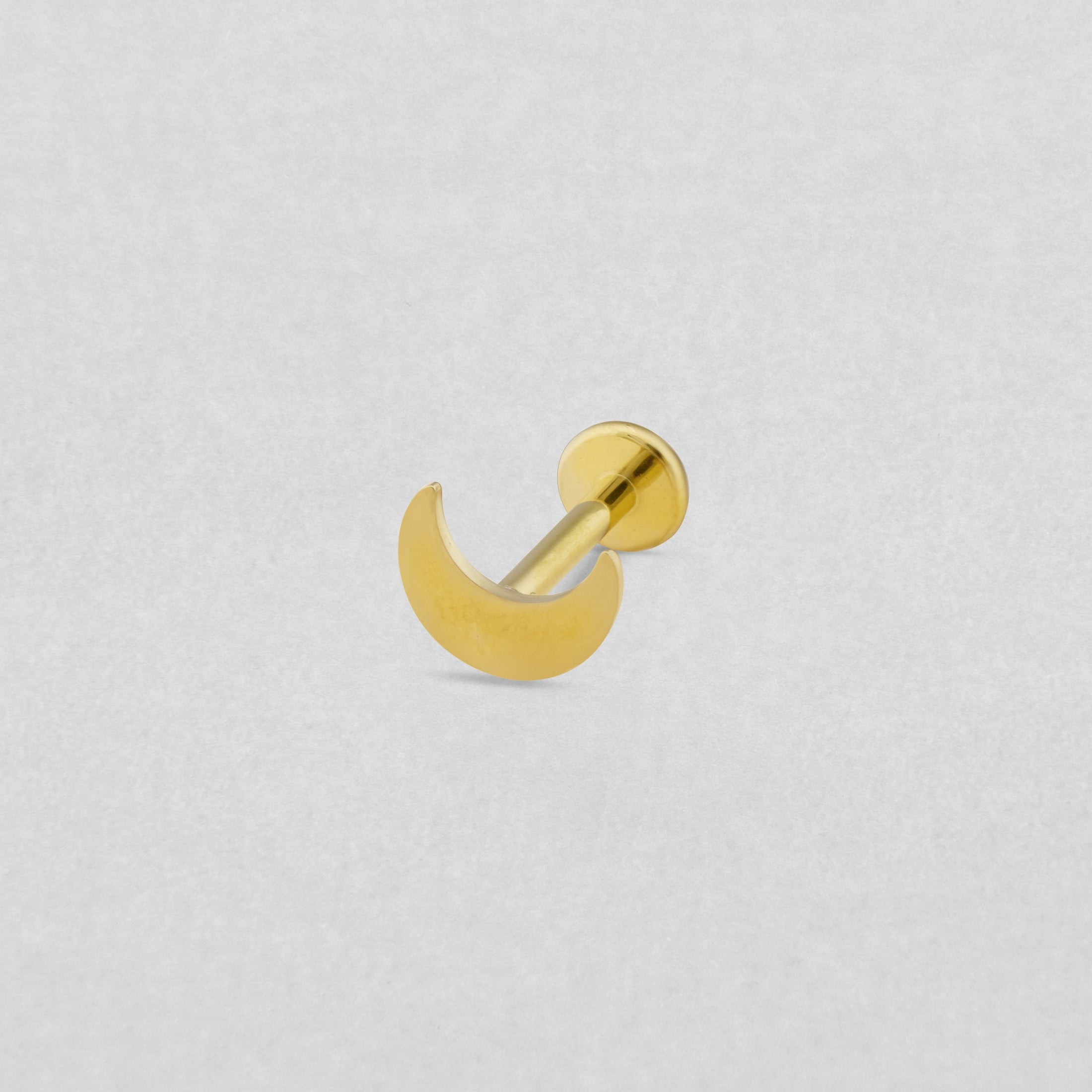 Das Modell «Luna liso» von Titanium-Noble Art ist ein halbmondförmiger goldener Knopf-Ohrstecker mit flacher Rückseite, ideal für Piercing-Liebhaber, auf hellgrauem Strukturhintergrund.