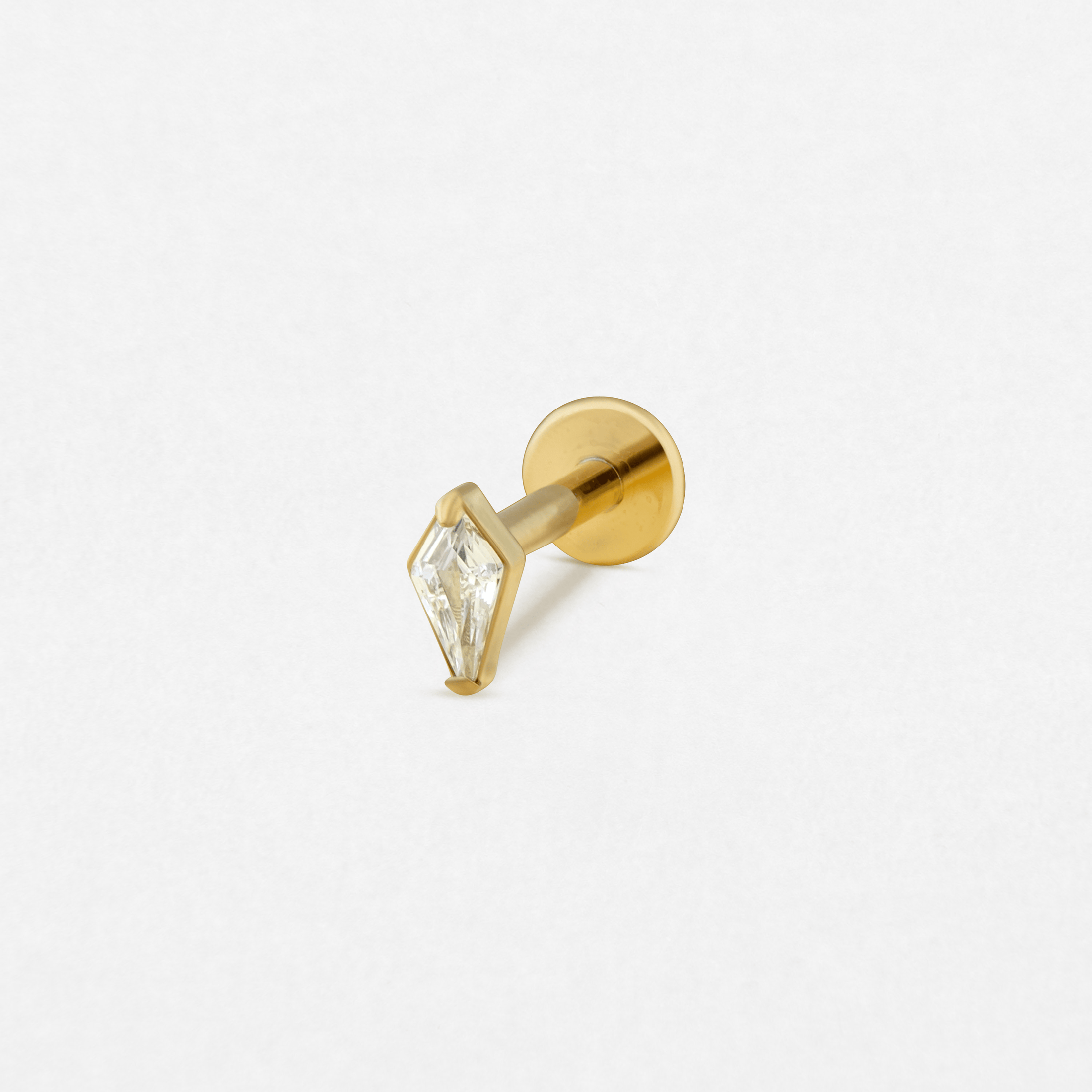 El modelo «Top Egan Gold» de Titanio-Noble Art es un pendiente de botón de oro con cierre plano y una piedra preciosa transparente en forma de rombo engastada en un bisel de oro, que se muestra sobre fondo blanco; ideal para quienes aprecian el estilo Noble Art tanto en joyería como en tatuajes.