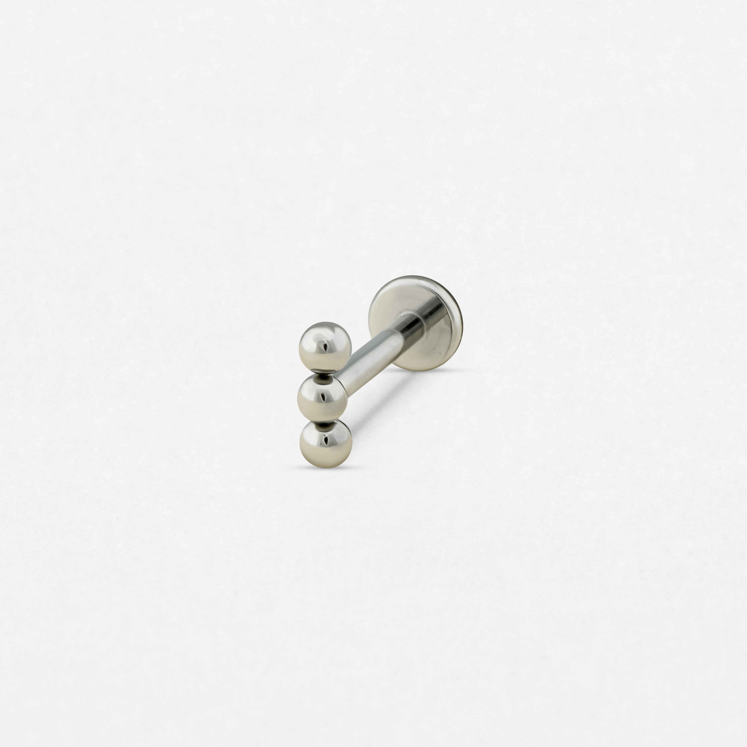 El gancho de pared Fenix plateado de Titanio-Noble Art cuenta con tres clavijas redondeadas dispuestas en línea vertical sobre una base circular, lo que destaca su diseño metálico minimalista sobre un fondo blanco liso.