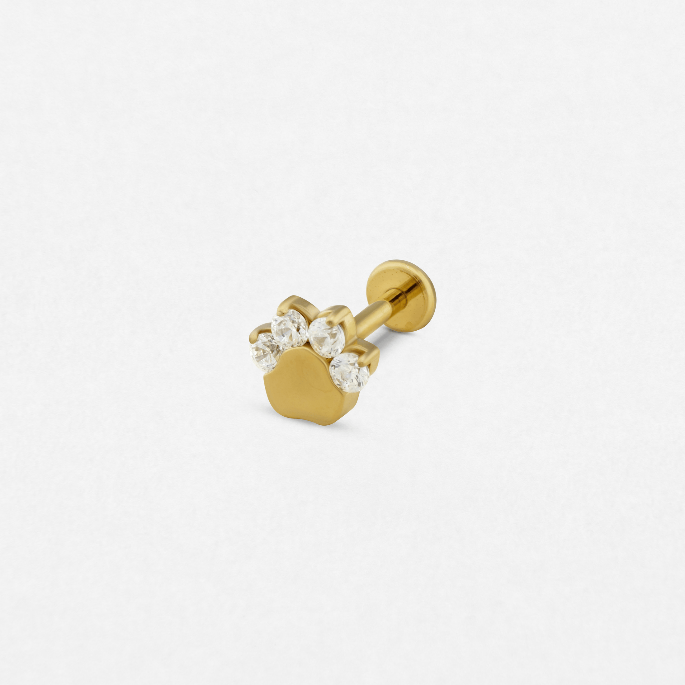 El pendiente de oro «Huella», de Titanio-Noble Art, presenta un diseño de huella de pata con cuatro piedras preciosas transparentes a modo de dedos, lo que pone de manifiesto una exquisita artesanía —que recuerda a un delicado tatuaje— sobre un fondo blanco liso.