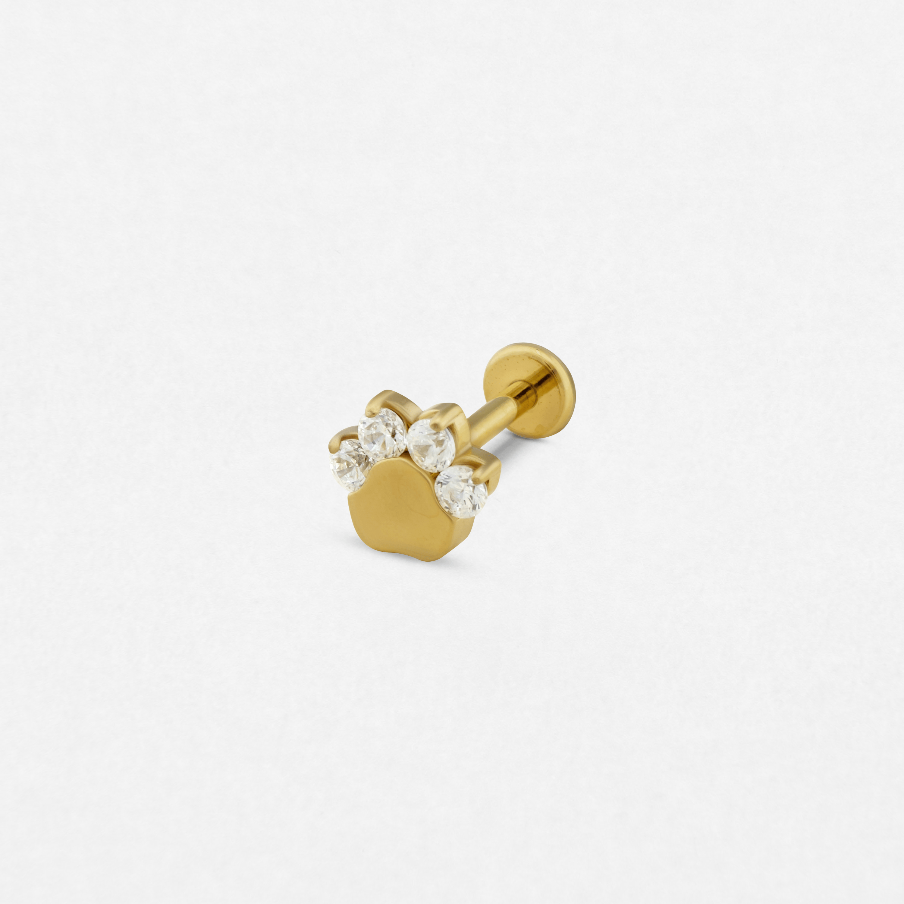 El pendiente de oro «Huella», de Titanio-Noble Art, presenta un diseño de huella de pata con cuatro piedras preciosas transparentes a modo de dedos, lo que pone de manifiesto una exquisita artesanía —que recuerda a un delicado tatuaje— sobre un fondo blanco liso.