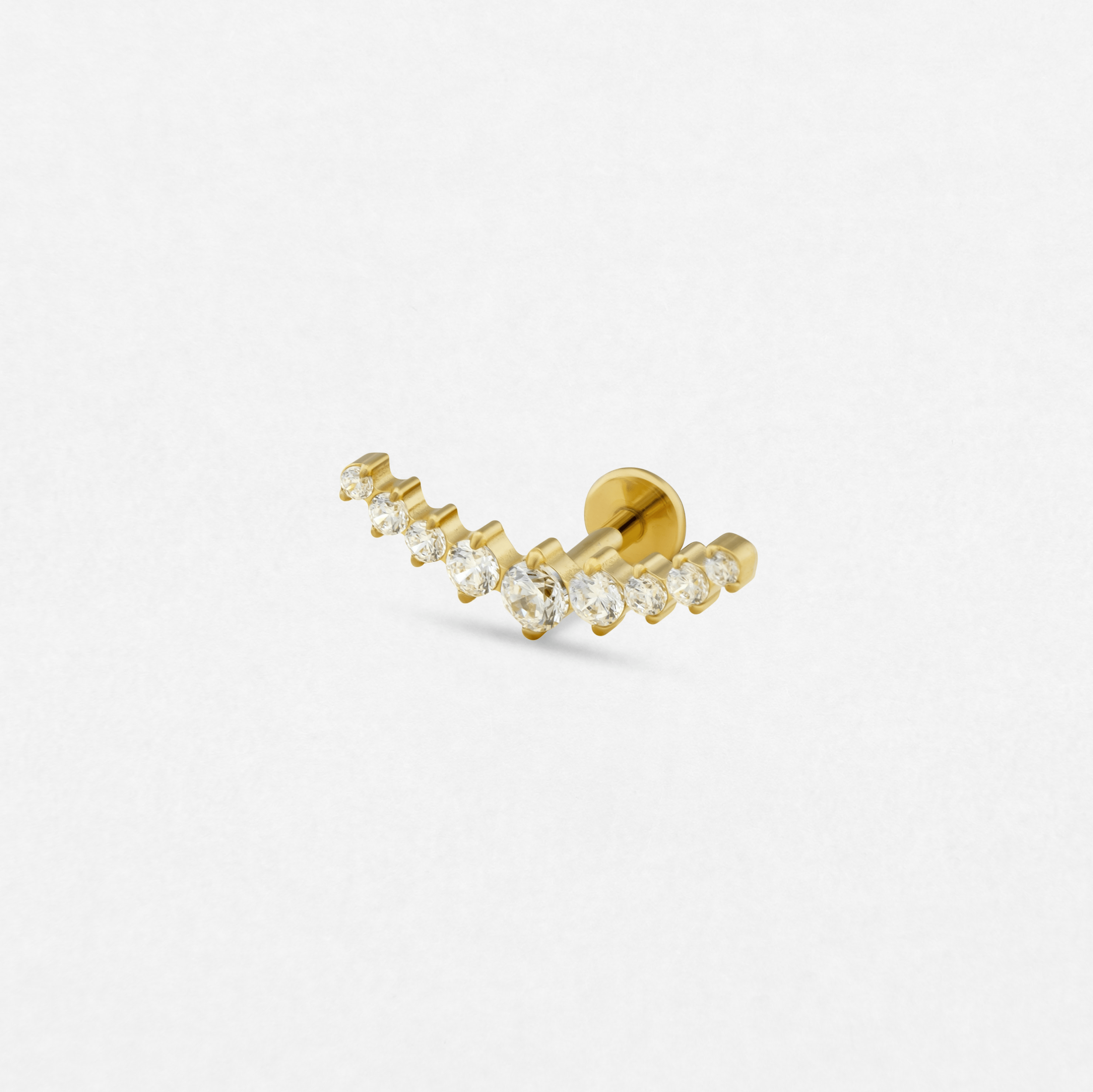 El pendiente «Leo» de Titanio-Noble Art es una pieza dorada con un diseño curvo y una hilera de piedras preciosas transparentes, perfecta para realzar tu piercing. Se muestra sobre un fondo blanco liso.