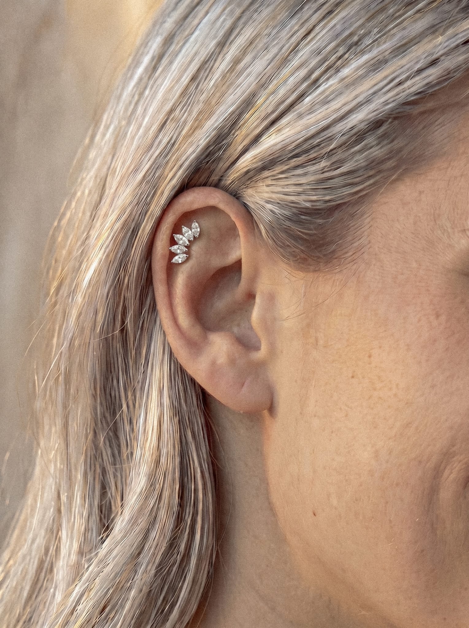 Gros plan sur l'oreille d'une personne aux cheveux blonds, mettant en valeur la boucle d'oreille « Titanio - Noble Art Marquise 5 cz » en argent, ornée de trois cristaux taille « corte marquise » sur le cartilage supérieur de l'oreille — idéale pour les looks modernes.