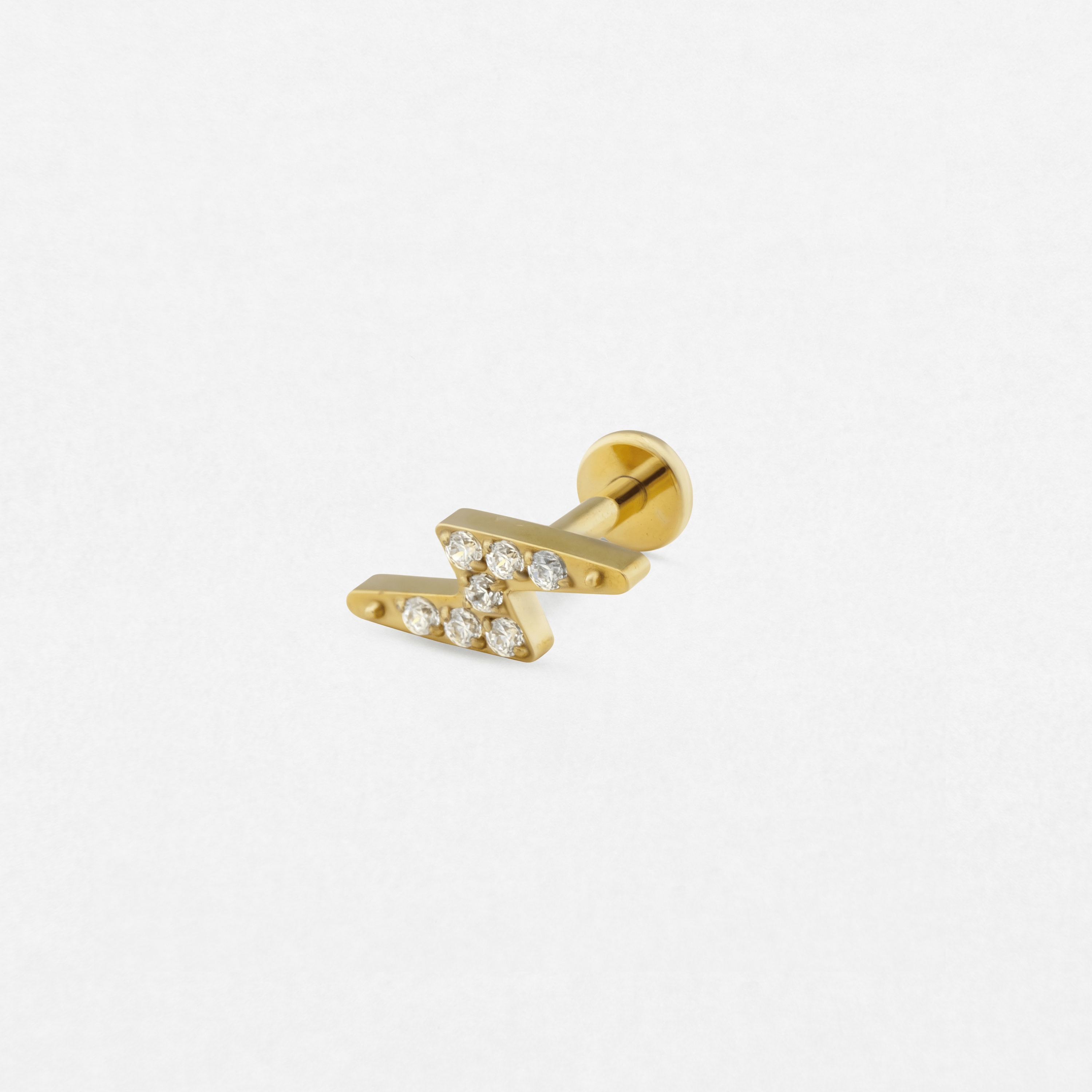 The Titanio-Noble Art Maya-style gold labret features a zigzag lightning bolt design with small clear gemstones, highlighting its elegance against a plain white background.