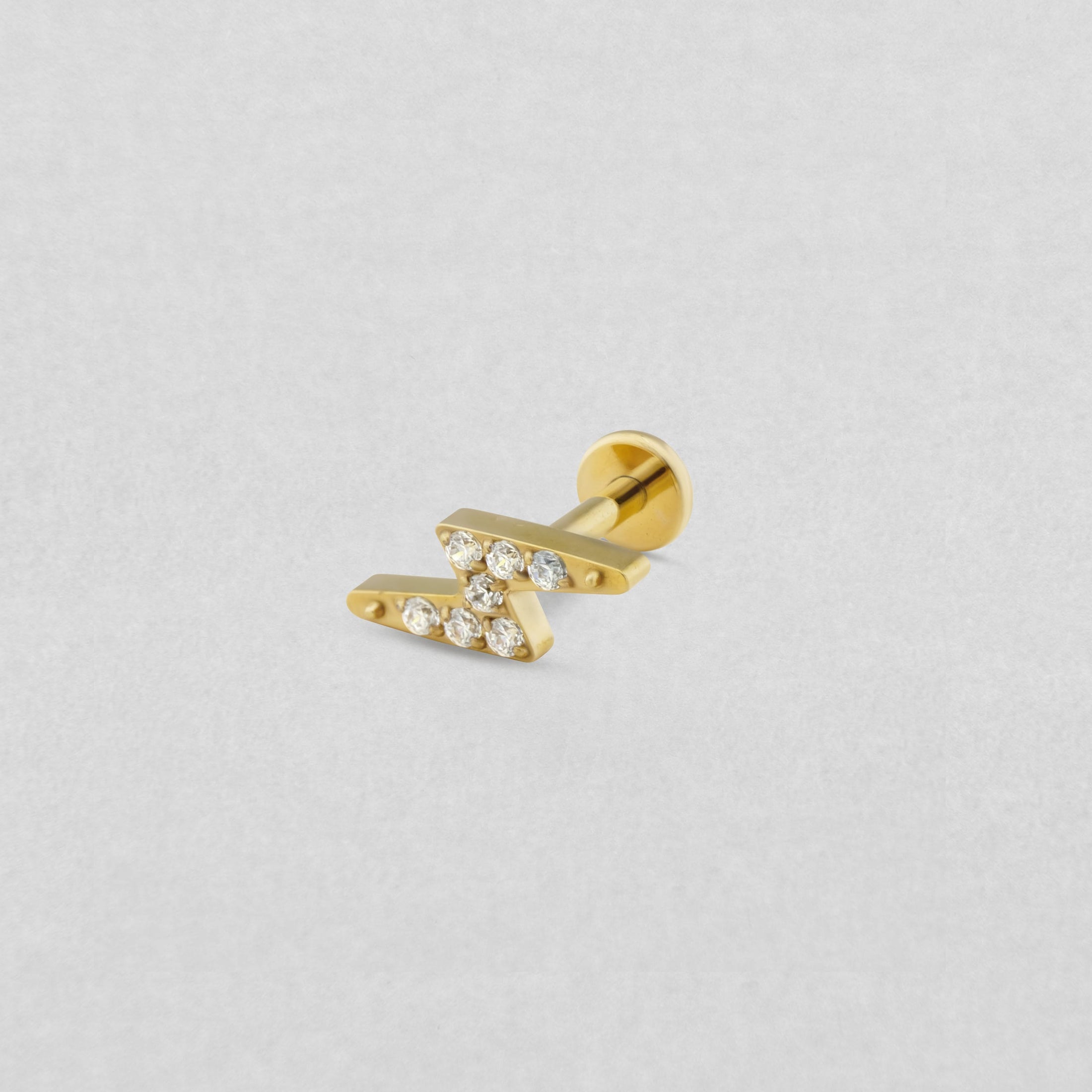 El modelo «Maya» de Titanio - Noble Art es un pendiente tipo barra en forma de barbell dorado que presenta dos barras paralelas y diagonales con brillantes diamantes redondos, ideal para un piercing refinado y que se muestra sobre un fondo gris claro.