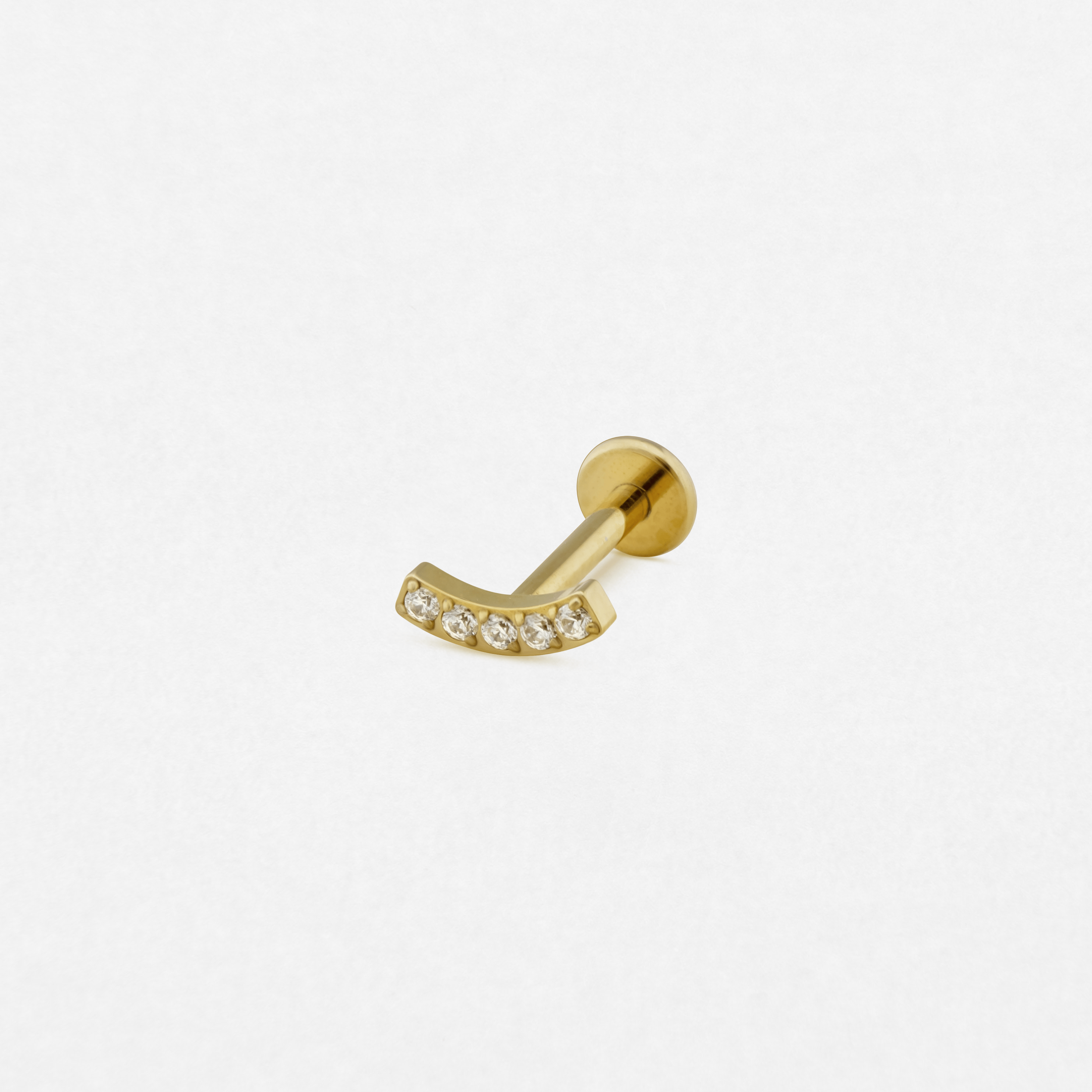 El pendiente «Mia Gold» de Titanio-Noble Art es un pendiente tipo barra curvada con seis pequeñas piedras preciosas transparentes engastadas a lo largo de la curva, que se muestra sobre un fondo blanco liso: una pieza tan refinada y llamativa como un tatuaje perfectamente realizado.