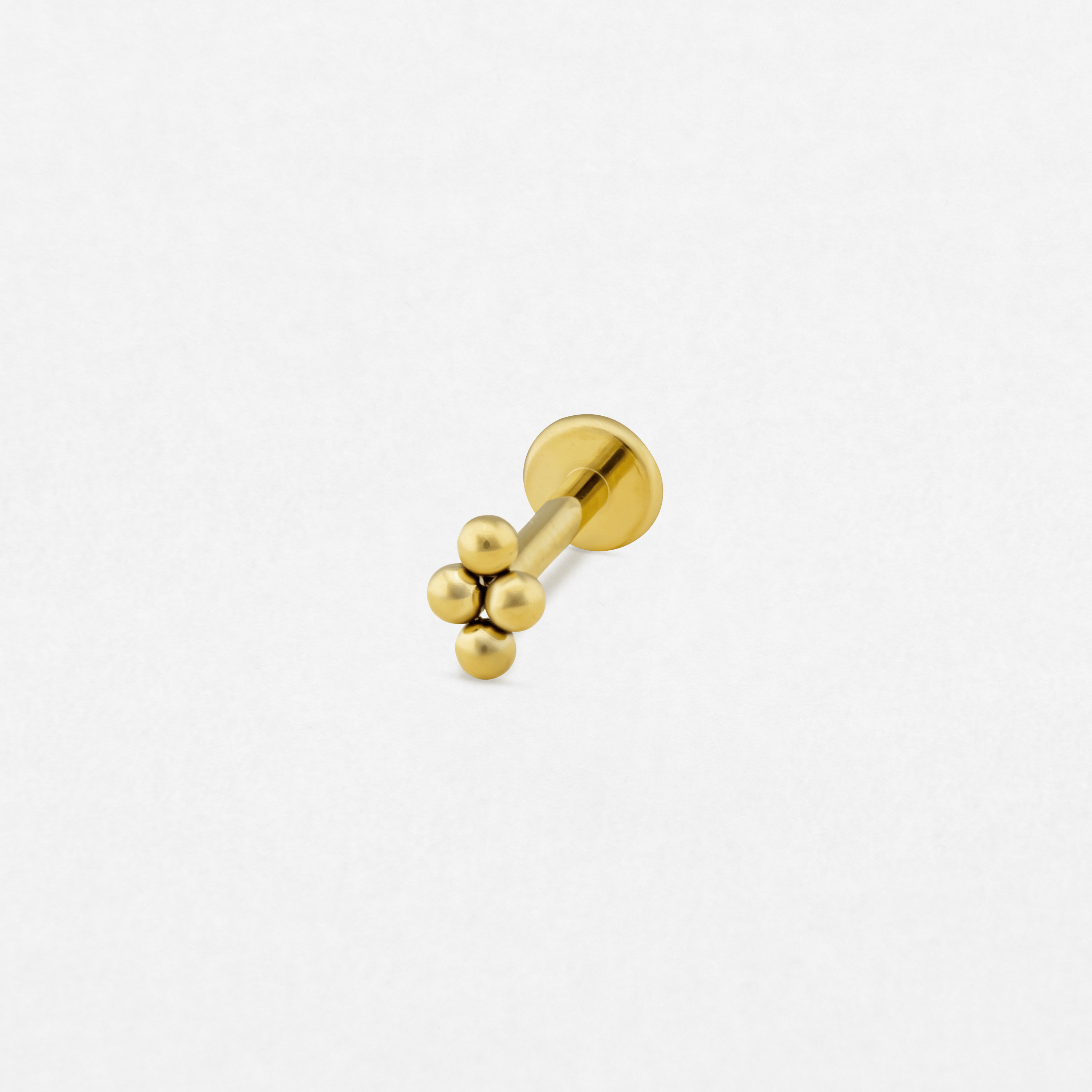 El pendiente labret NIDO GOLD de NOBLE ART BEAUTY SOCIEDAD LIMITADA presenta cuatro esferas doradas agrupadas en un extremo; se muestra sobre un fondo blanco liso y es un ejemplo de estilo refinado.