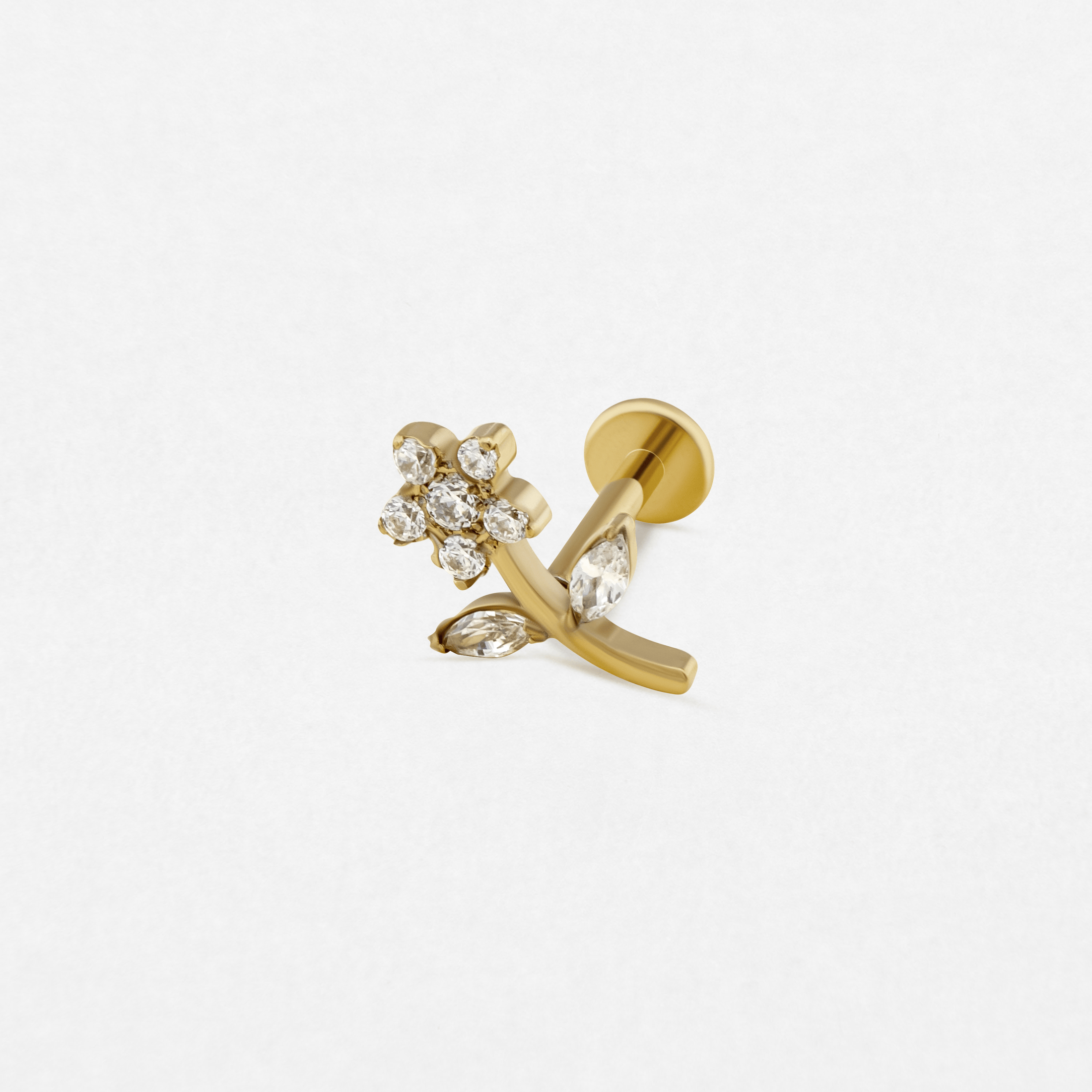 El pendiente de botón «Selena» de Titanio-Noble Art presenta una flor dorada con un tallo curvado, decorada con piedras preciosas transparentes en los pétalos y las hojas. Ideal para los amantes de los piercings. Se muestra sobre un fondo blanco liso.
