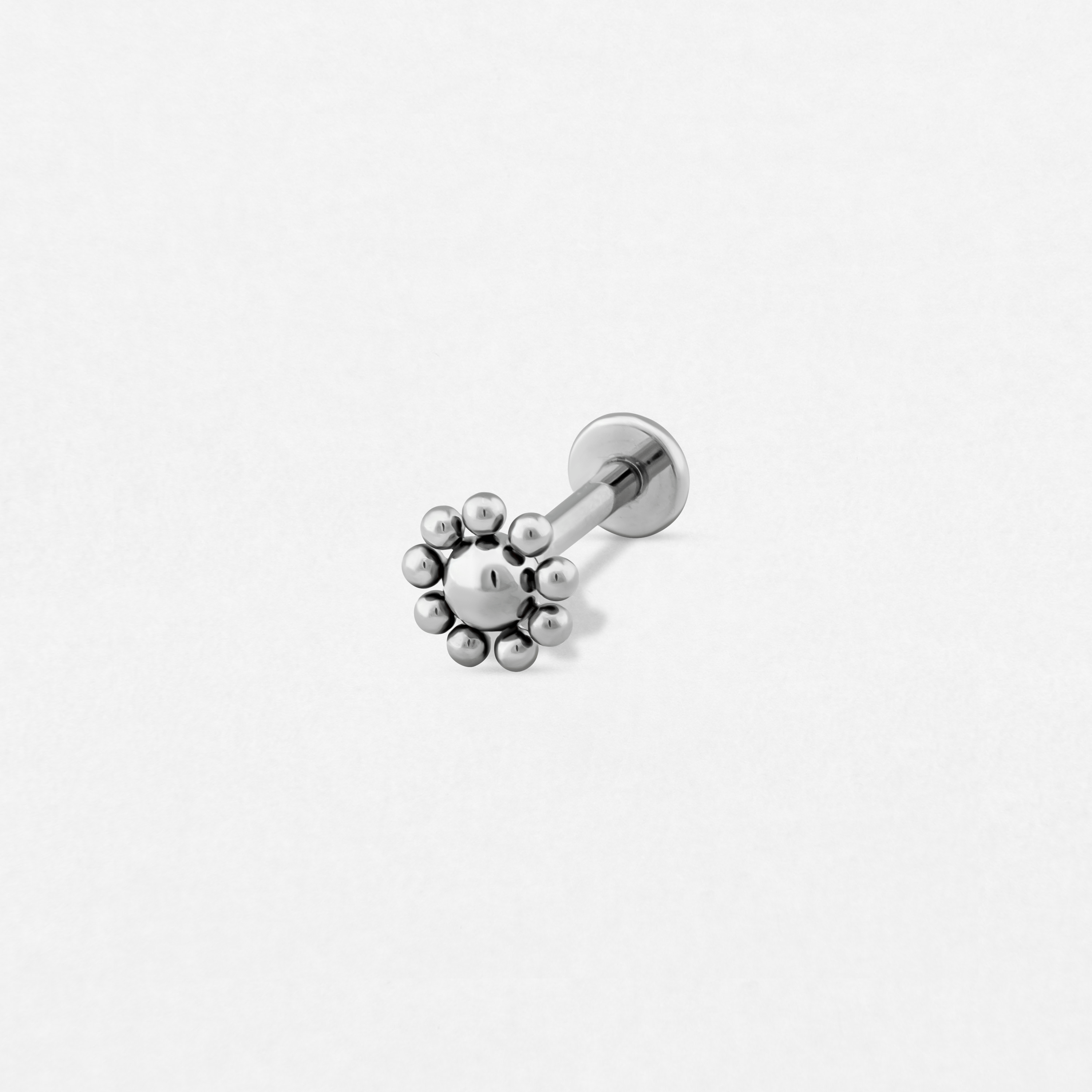 El pendiente de botón «Sun Flower» de Titanio-Noble Art presenta una bola central con detalles más pequeños en un diseño plateado inspirado en una flor. Presentado sobre un fondo blanco liso, es perfecto para cualquier tipo de piercing y encarna la elegancia de Noble Art.