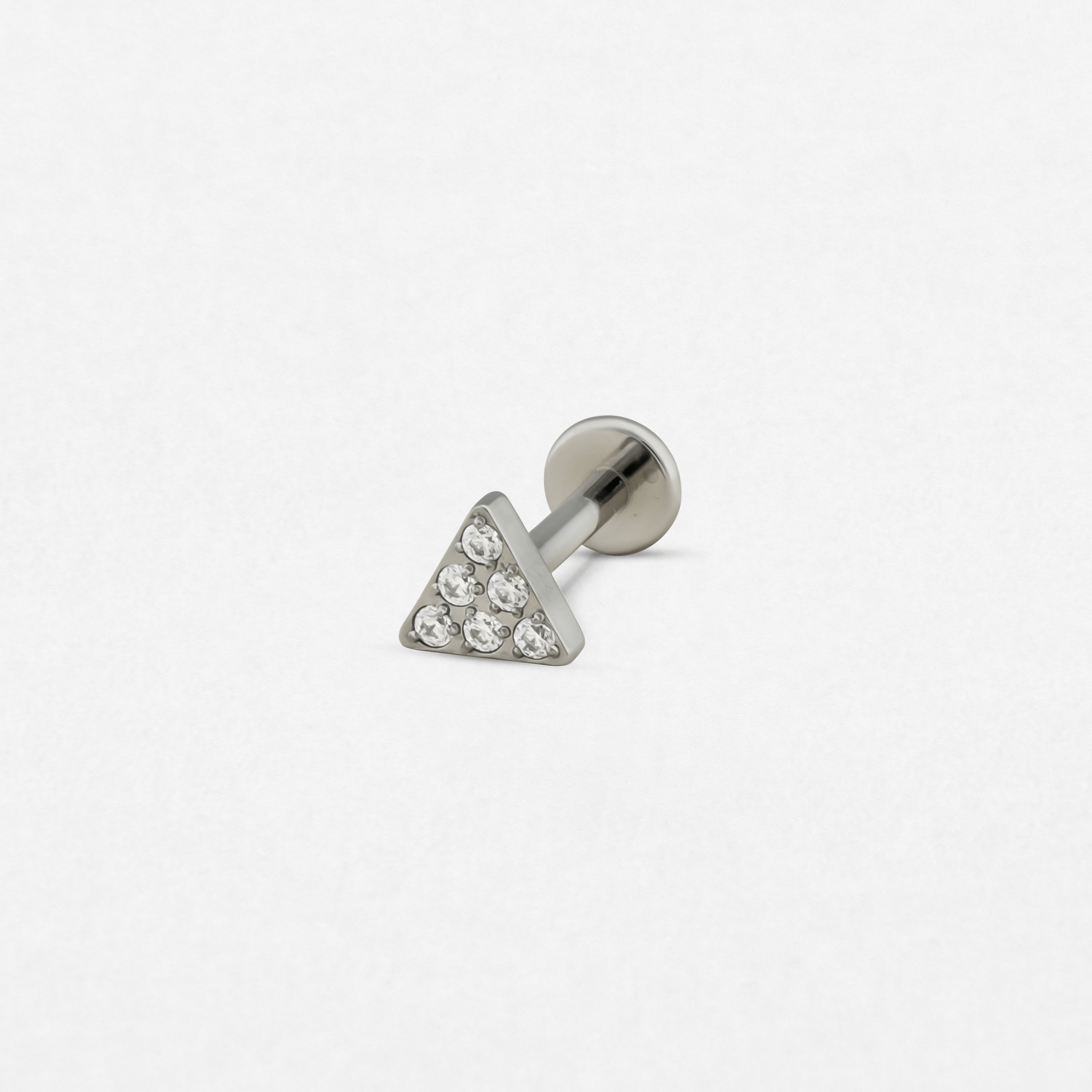 El modelo «Trianglue CZ» de Titanio-Noble Art es un pequeño pendiente de botón de plata con una parte frontal triangular adornada con seis piedras preciosas transparentes y una parte trasera plana, que se muestra sobre un fondo blanco liso.