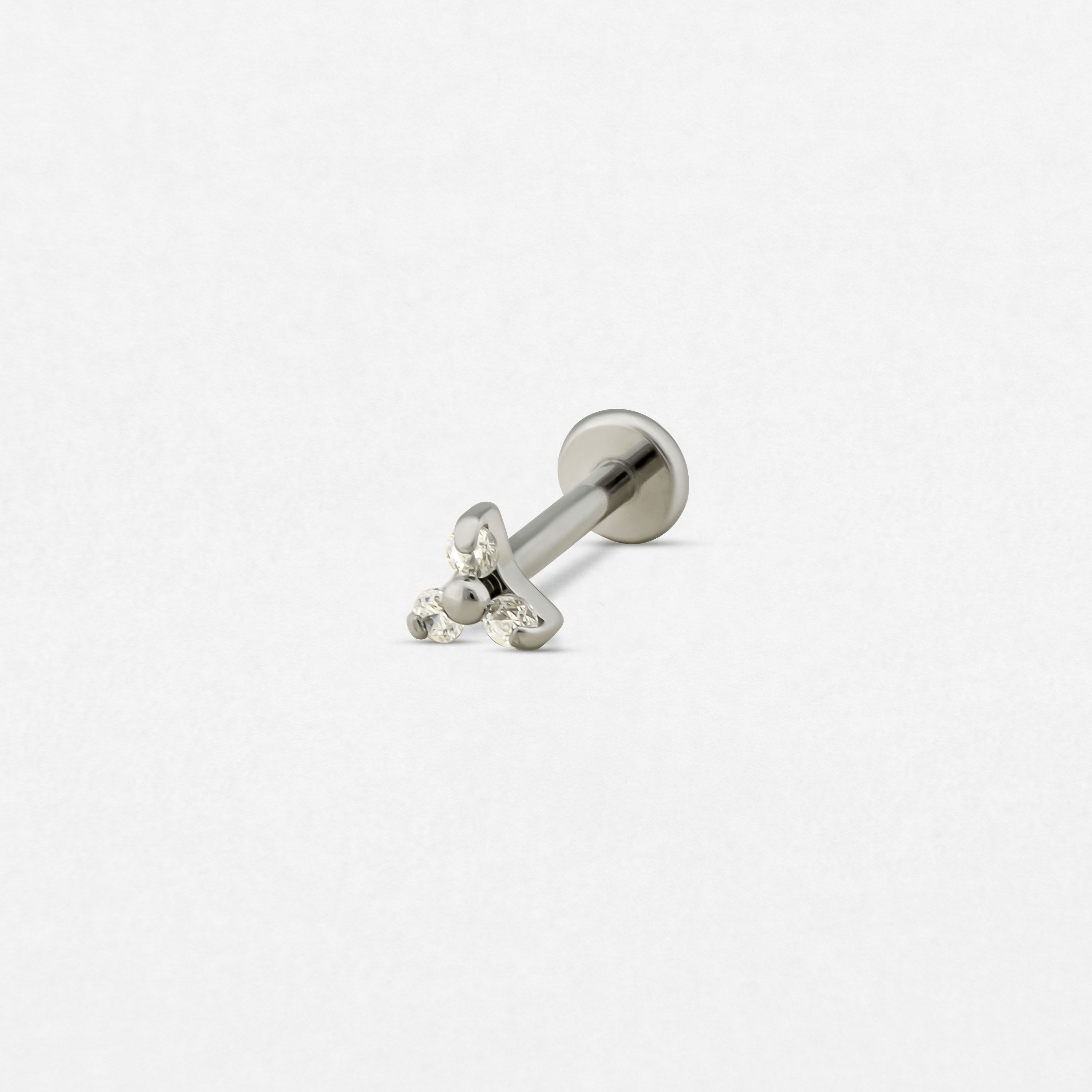 El «Titanio- Noble Art Trinity cz blanco» es un pendiente tipo labret de plata con cierre plano y un conjunto de tres piedras preciosas transparentes en la parte delantera, que se muestra sobre un fondo blanco.