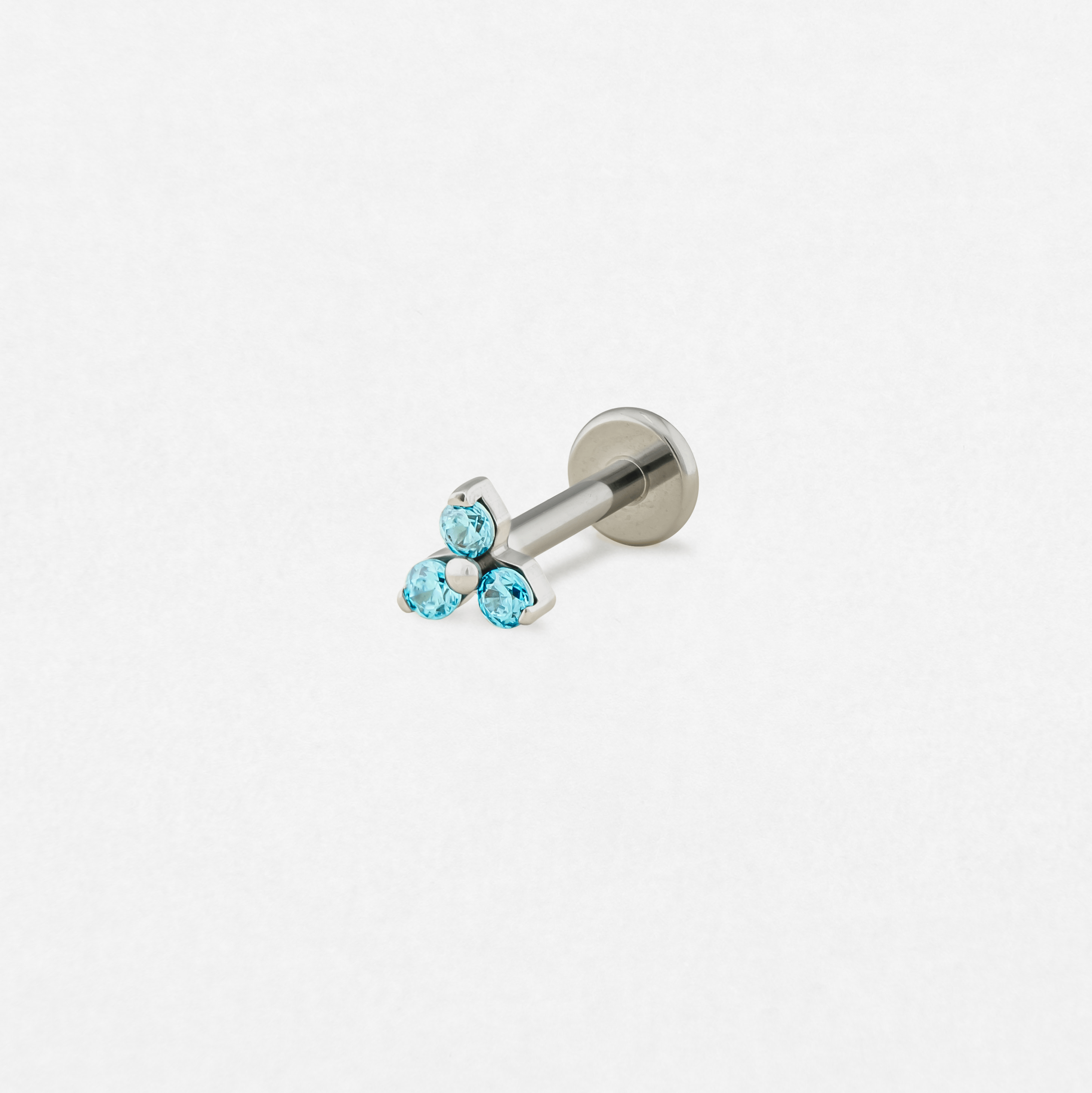 El pendiente de labret «Trinity cz» de Titanio-Noble Art cuenta con tres piedras preciosas azules redondas dispuestas en forma de triángulo en su extremo plano, lo que lo convierte en una pieza perfecta para tu colección de piercings. Presentado sobre un fondo blanco, encarna la elegancia de Noble Art.