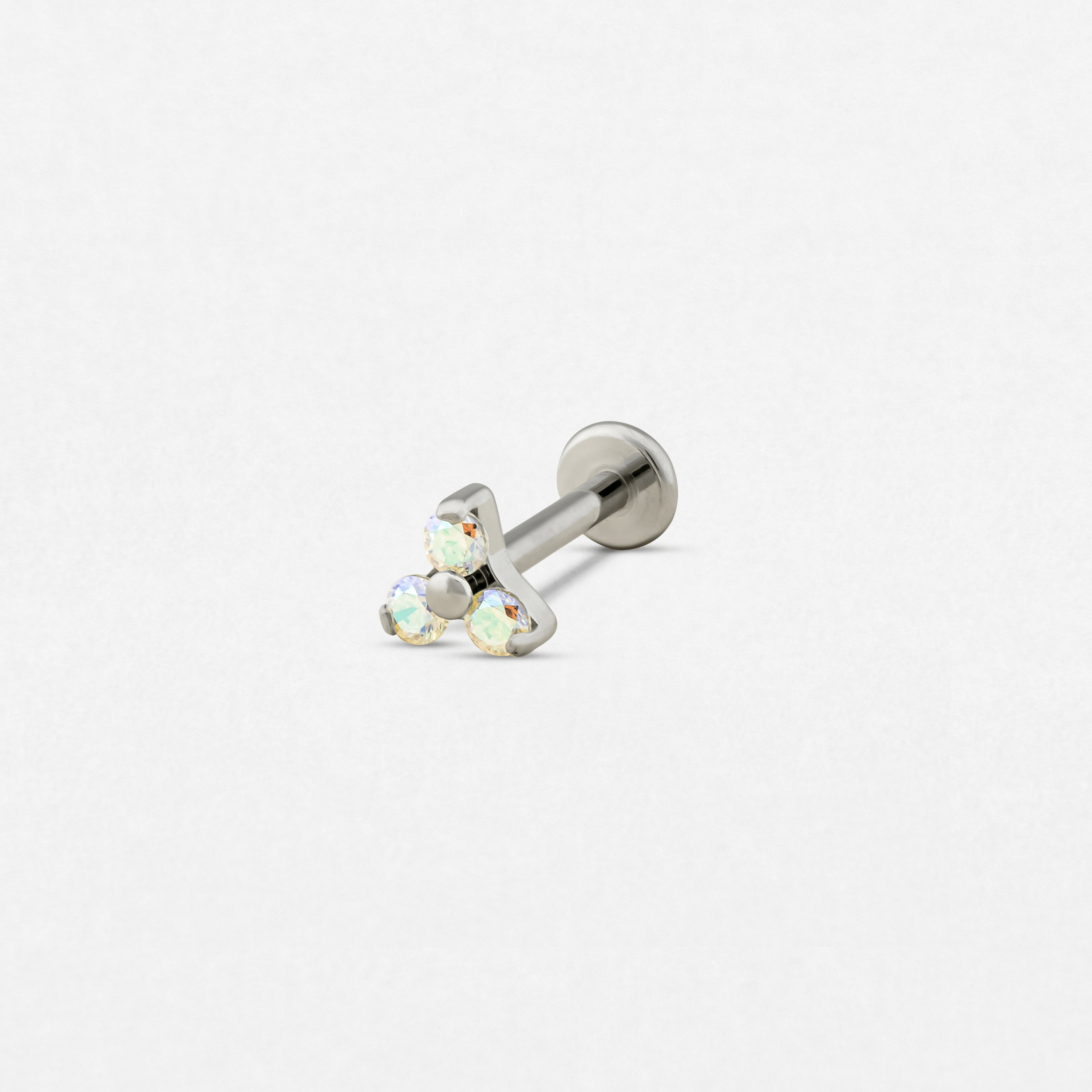 El modelo «Trinity cz opalo blanco» de Titanio-Noble Art es un pendiente de botón de plata con tres piedras preciosas iridiscentes dispuestas en forma de triángulo, que se muestran sobre un fondo blanco liso, perfecto para tu piercing Noble Art.