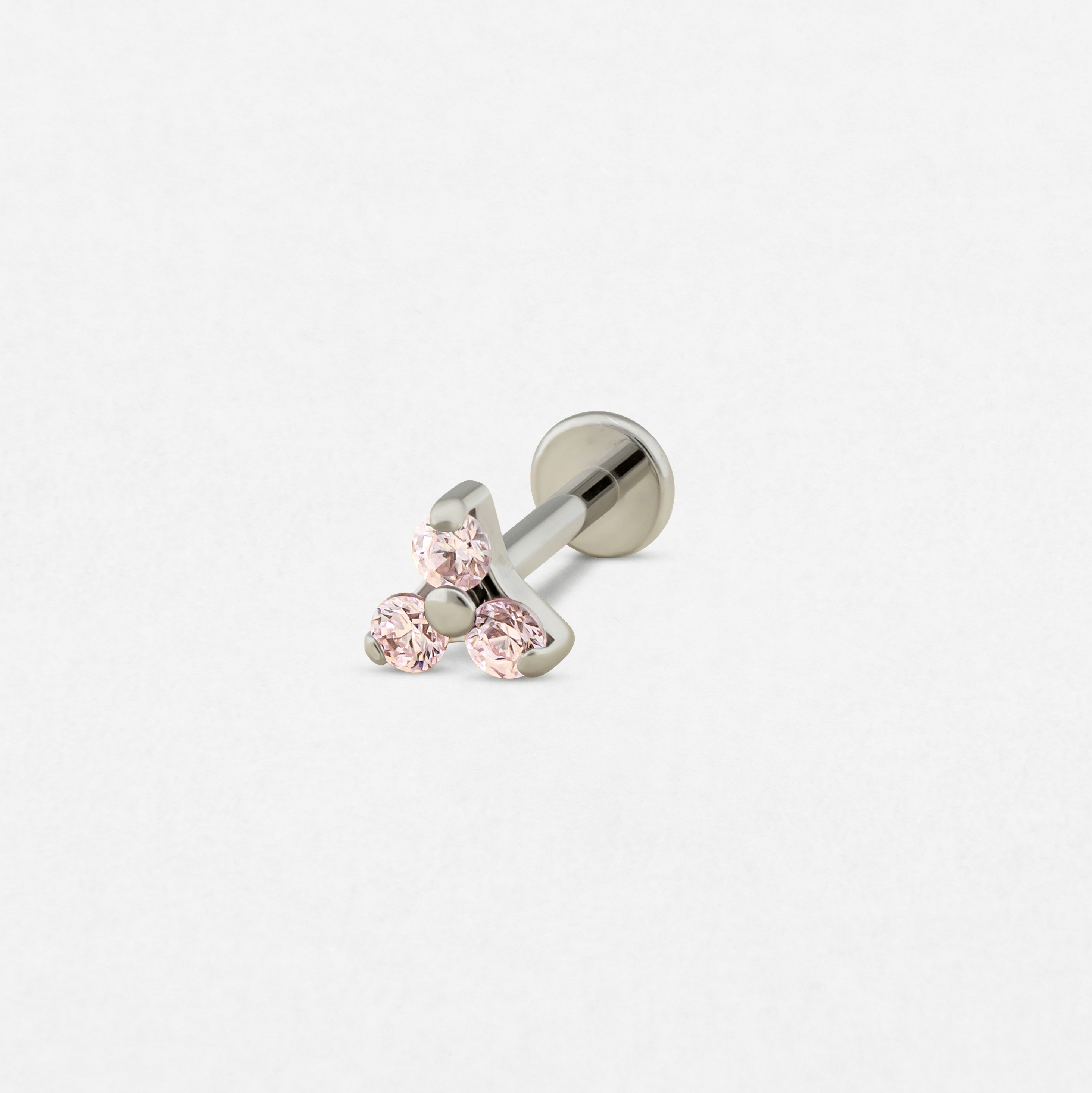 El modelo TRINITY CZ ROSA de Titanio-Noble Art es un pendiente tipo labret de plata con tres piedras redondas de color rosa claro dispuestas en forma de triángulo, ideal para los amantes de los piercings.