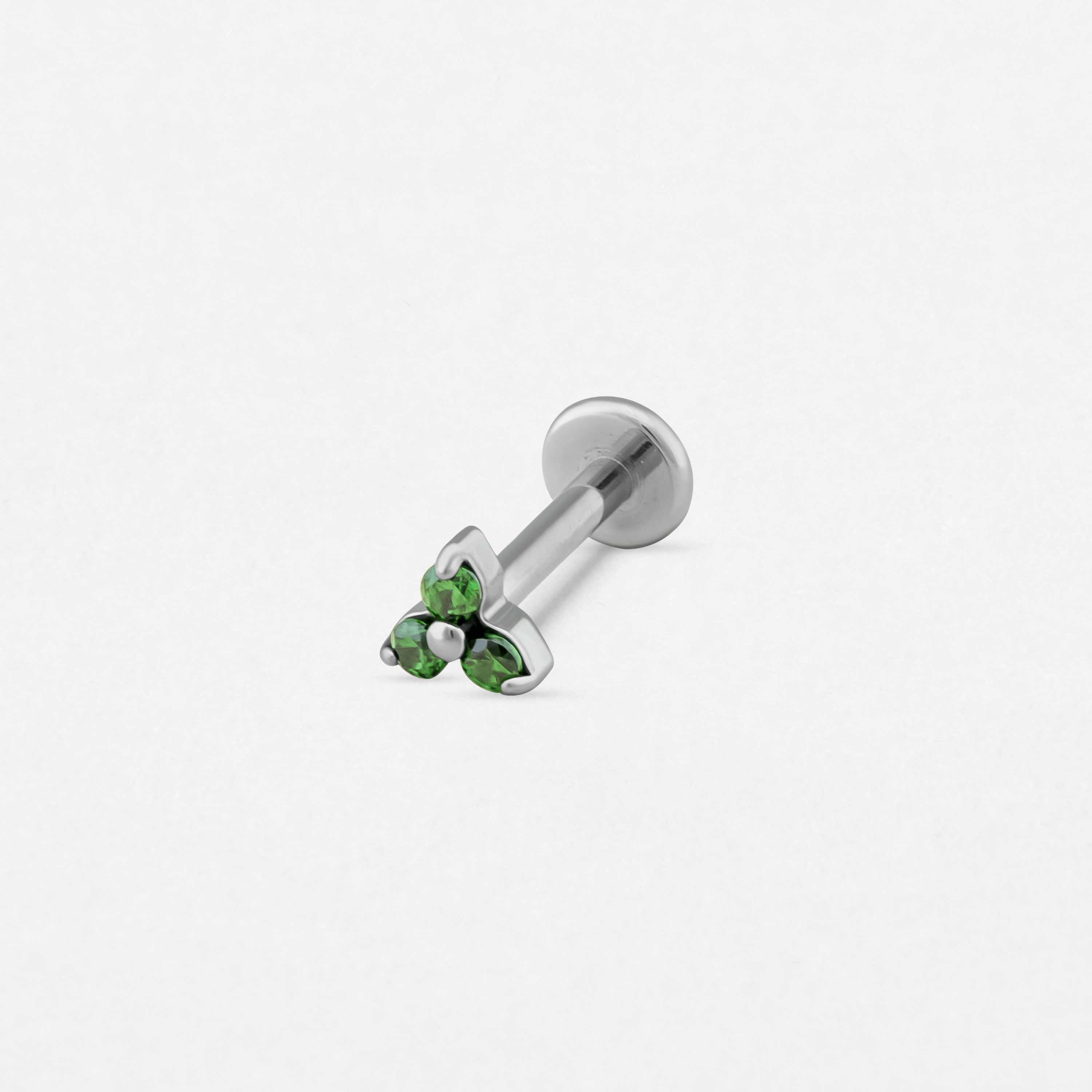 El «Trinity cz verde» de Titanio-Noble Art es un pendiente tipo labret de plata con cierre plano, adornado con tres piedras preciosas verdes dispuestas en forma de triángulo, ideal para tu piercing.