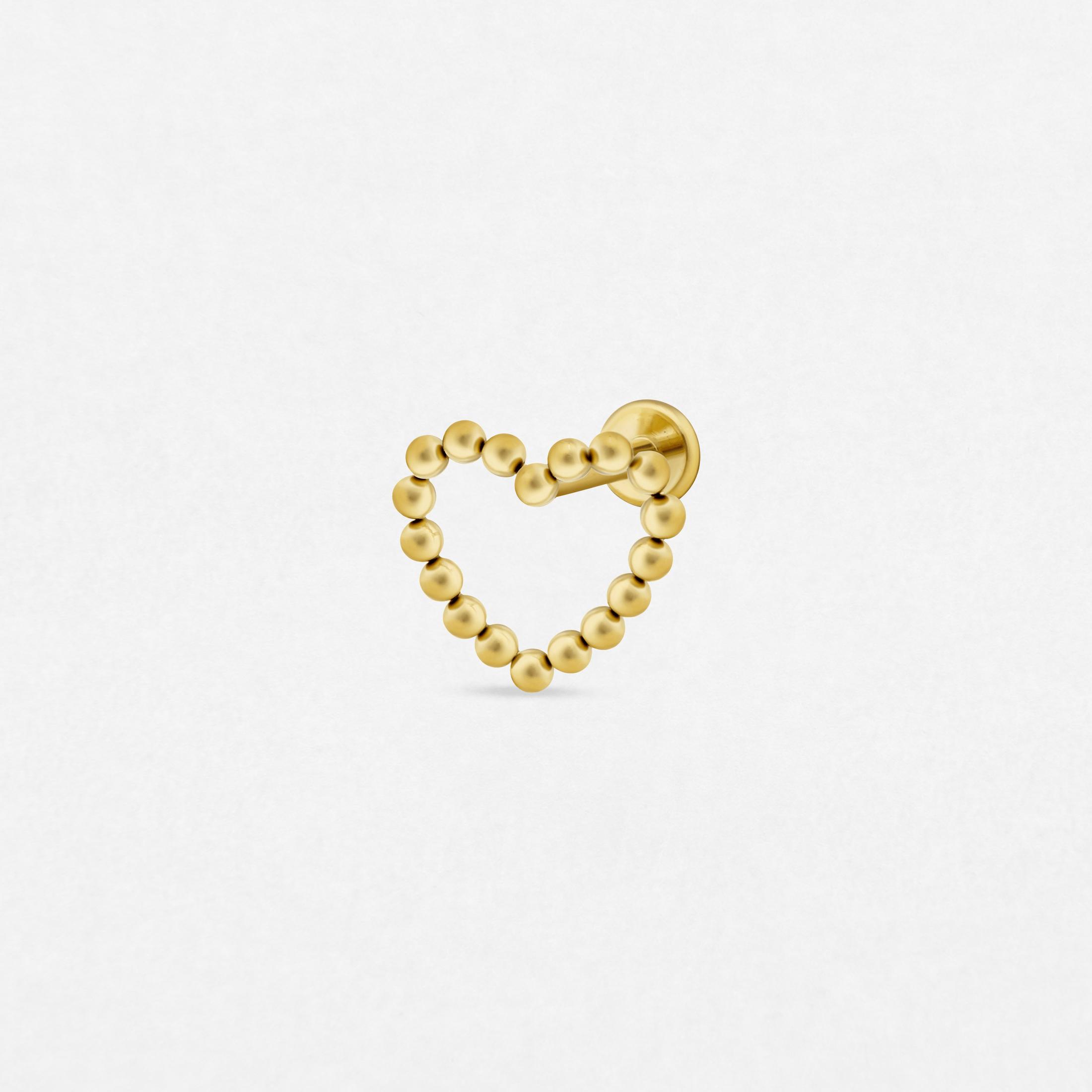 El pendiente «Amar Gold» de Titanio-Noble Art presenta una forma de corazón elaborada con pequeñas cuentas doradas y un cierre sencillo, ideal para tu piercing favorito, que destaca sobre un fondo blanco liso.