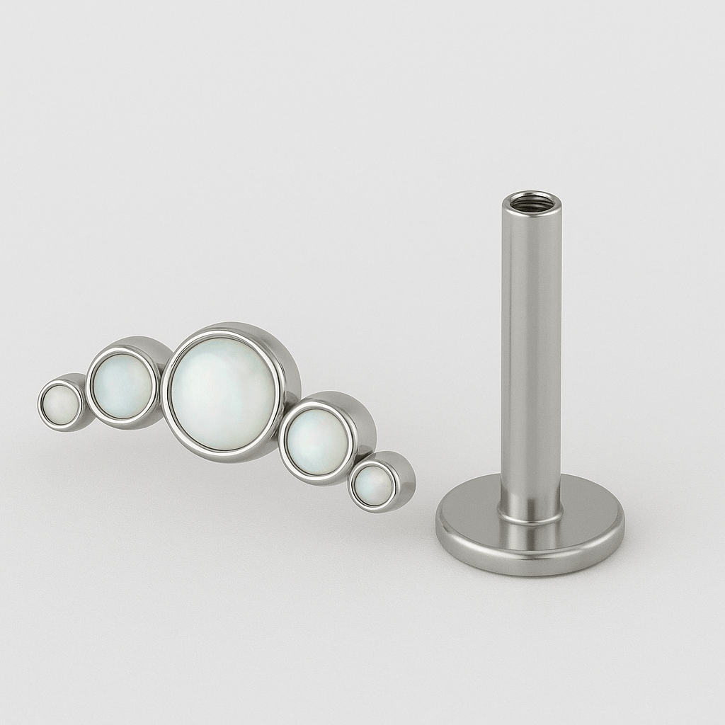 El modelo CLUSTER OPALO BLANCO de NOBLE ART BEAUTY SOCIEDAD LIMITADA cuenta con cinco piedras redondas opalescentes dispuestas en forma de arco y una barra de plata a juego, ideal para completar tu colección de piercings. Se muestra sobre un fondo blanco.